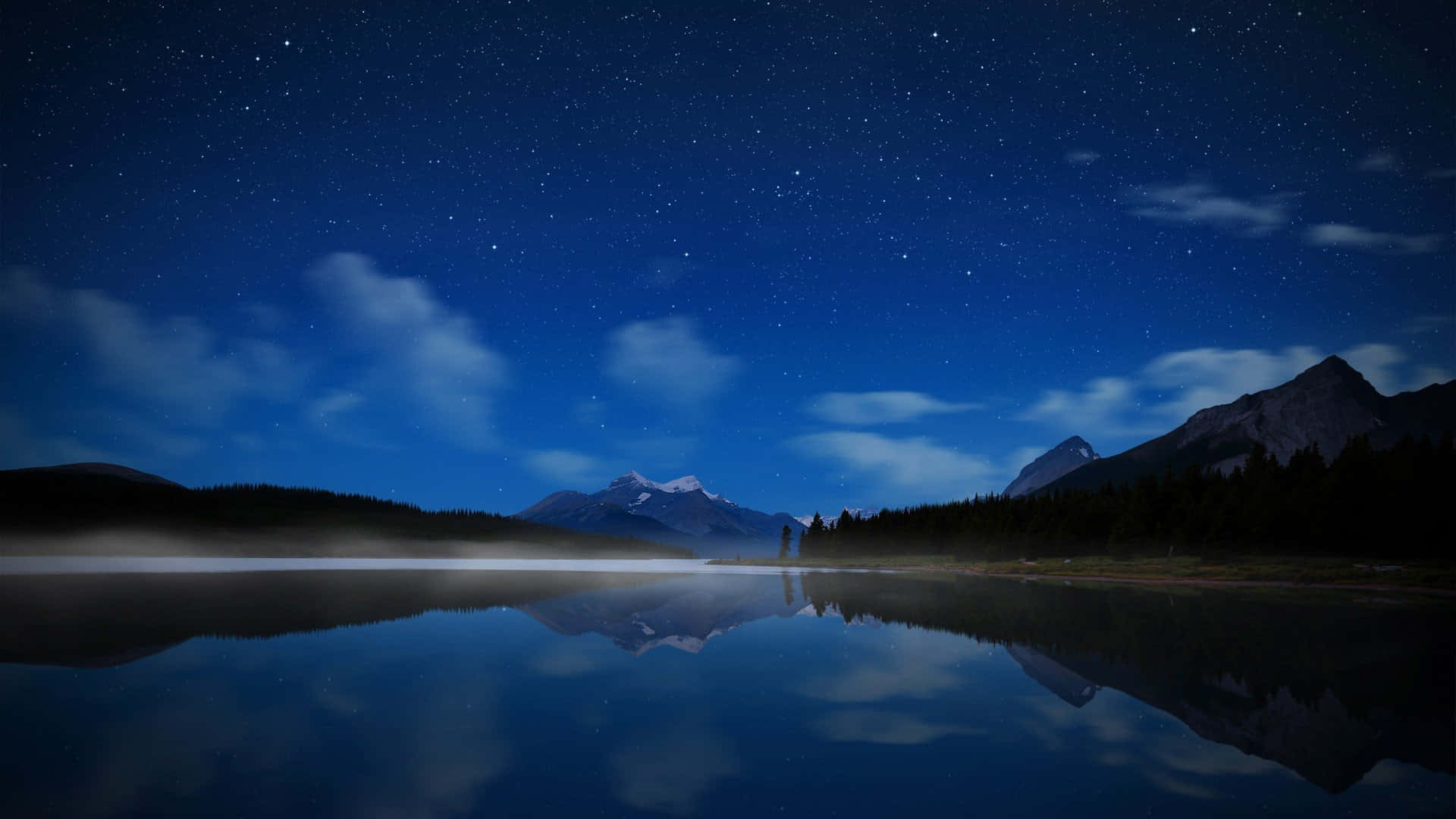 Night Time 桌布 壁紙 — 繁星點點的夜空完美地倒映在平靜的湖面上，四周環繞著黑暗的山脈和森林。