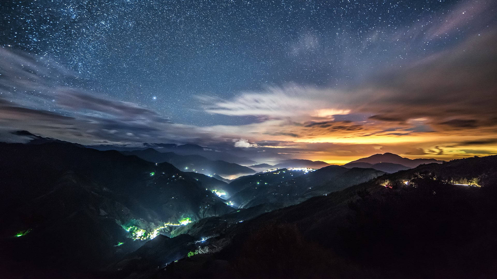 在繁星點點的夜空和五彩雲朵下的山谷燈光。