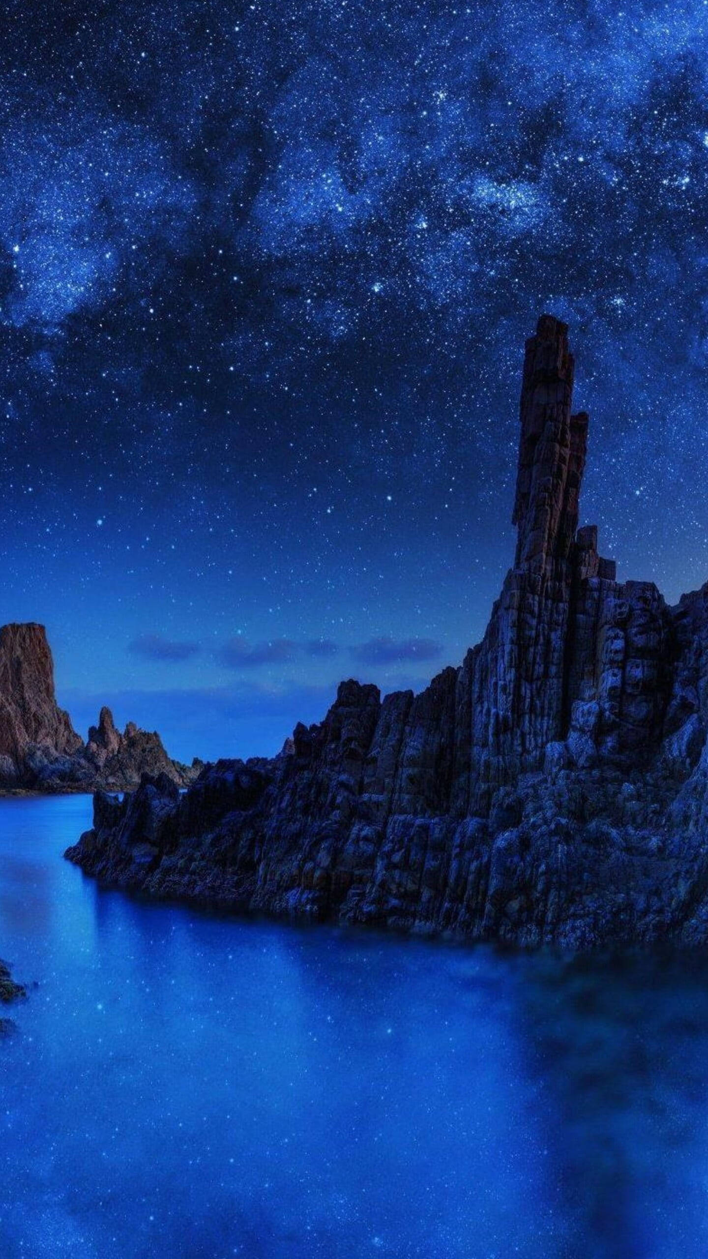 Beautiful Landscape 桌布 壁紙 — 繁星點點的夜空拱起在崎嶇的深色岩石 formations 旁邊，平靜的藍色水面反射著天體的光芒。