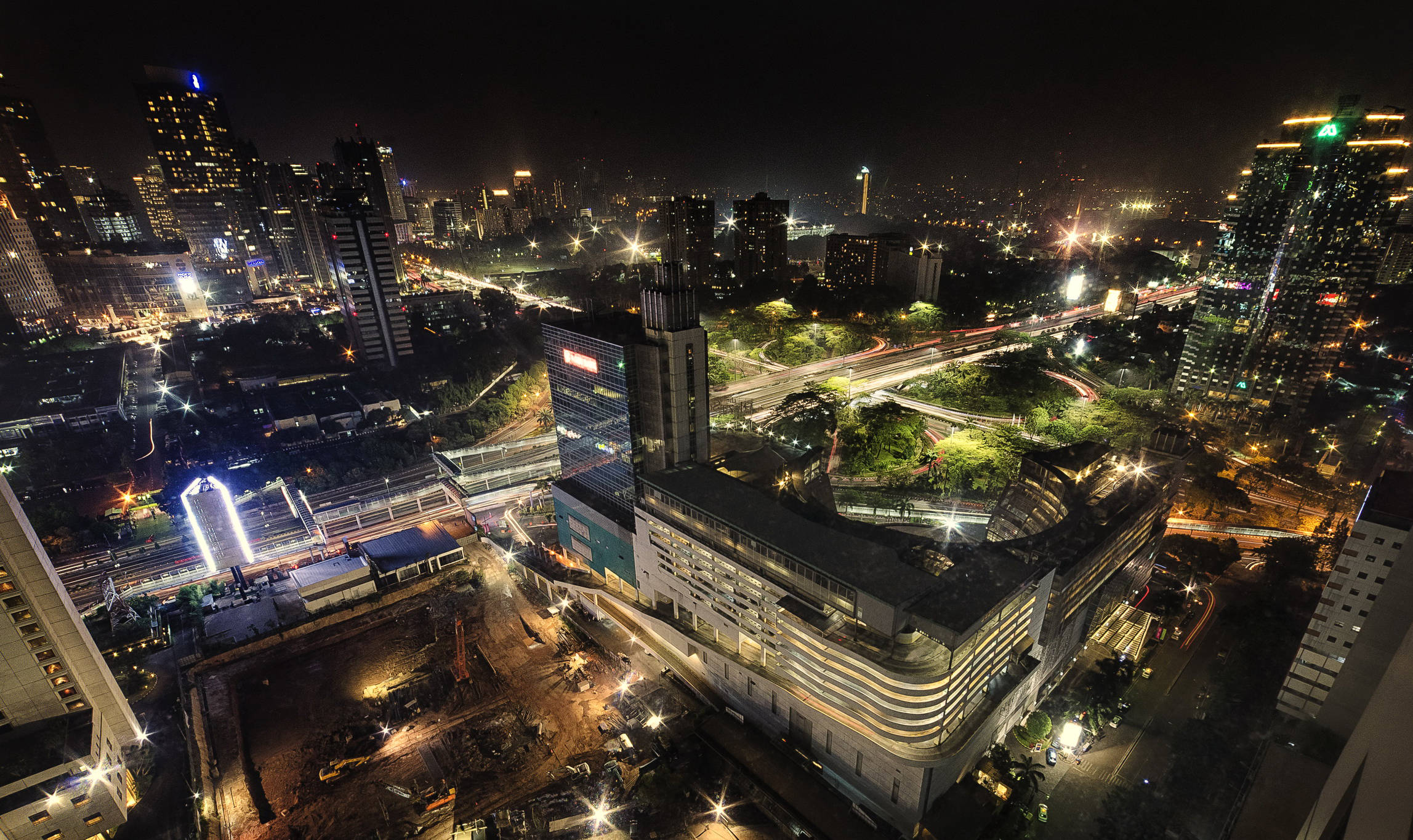印尼 桌布 壁紙 — 繁華城市景觀的空中夜景，閃爍的摩天大樓和照明的高速公路蜿蜒穿過密集的城市建築。