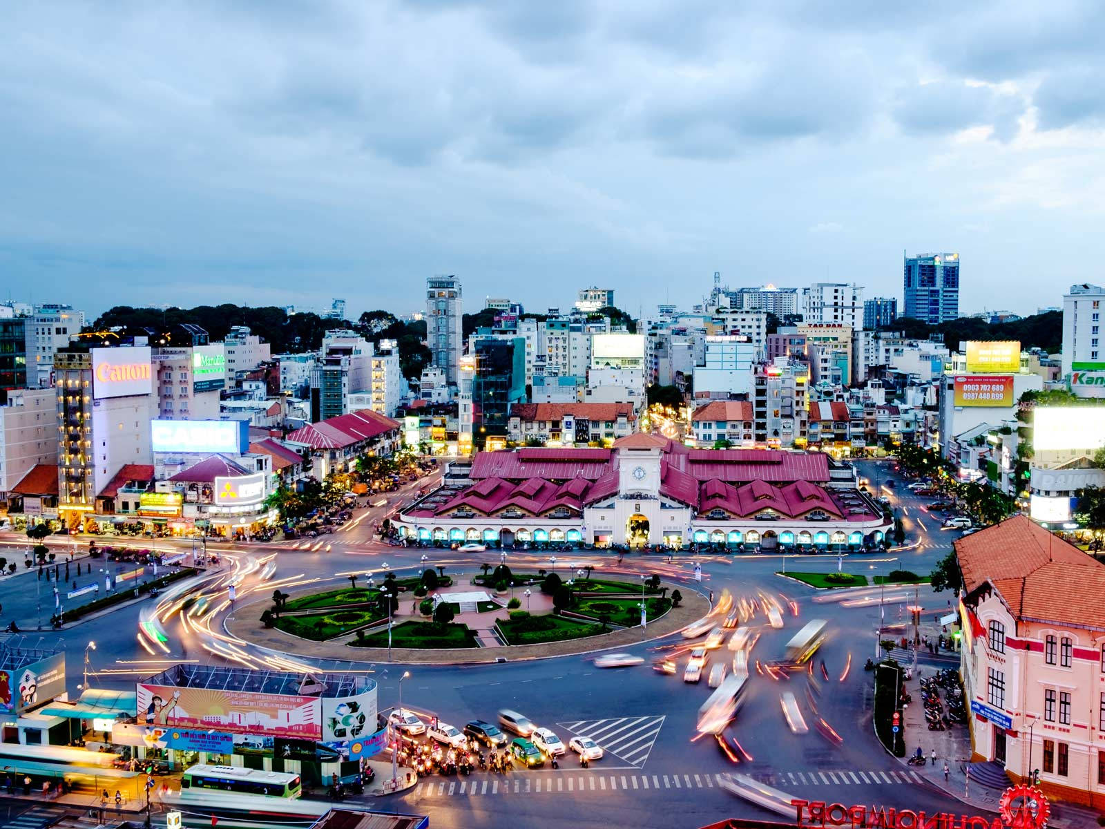 Ho Chi Minh City 桌布 壁紙 — 繁華的城市景觀在黃昏時分，車流的光跡在中央圓環周圍旋轉，天空多雲。