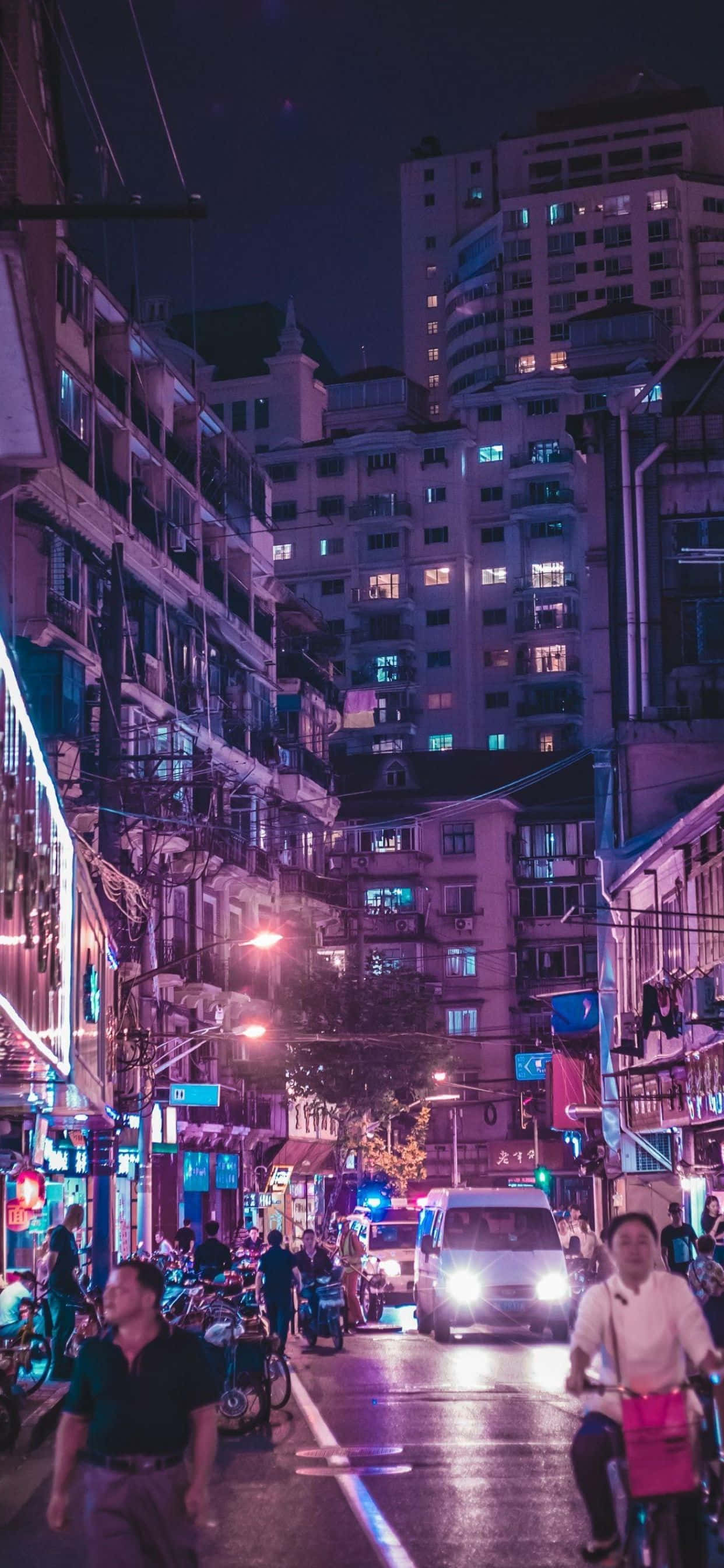 iPhone Xs Max 桌布 壁紙 — 繁華的霓虹燈城市小巷夜景，有行人、騎腳踏車者和發光的商店櫥窗，天空漆黑一片。