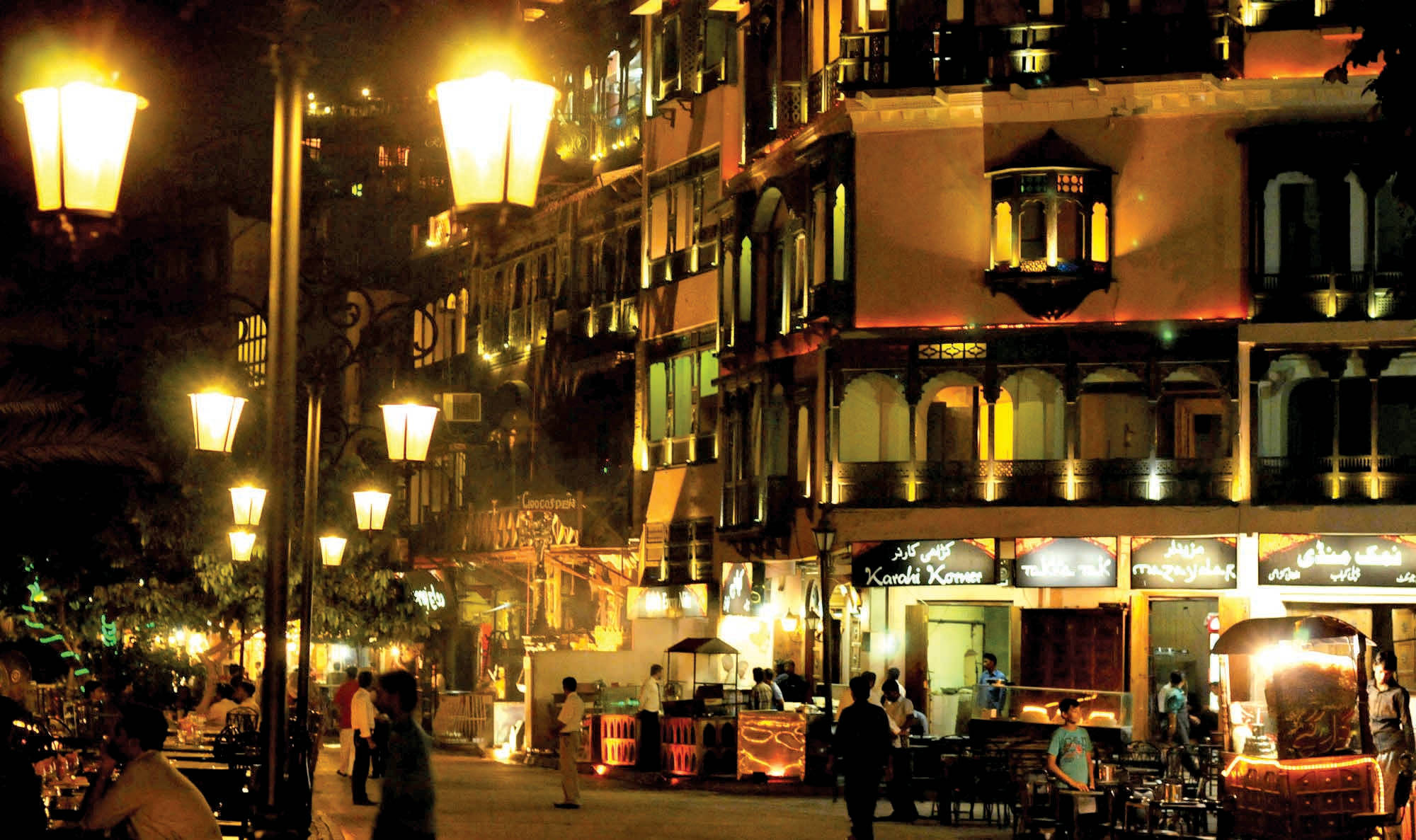 拉合爾 桌布 壁紙 — 繁華街道上的熱鬧夜景，溫暖照明的殖民風格建築和行人。