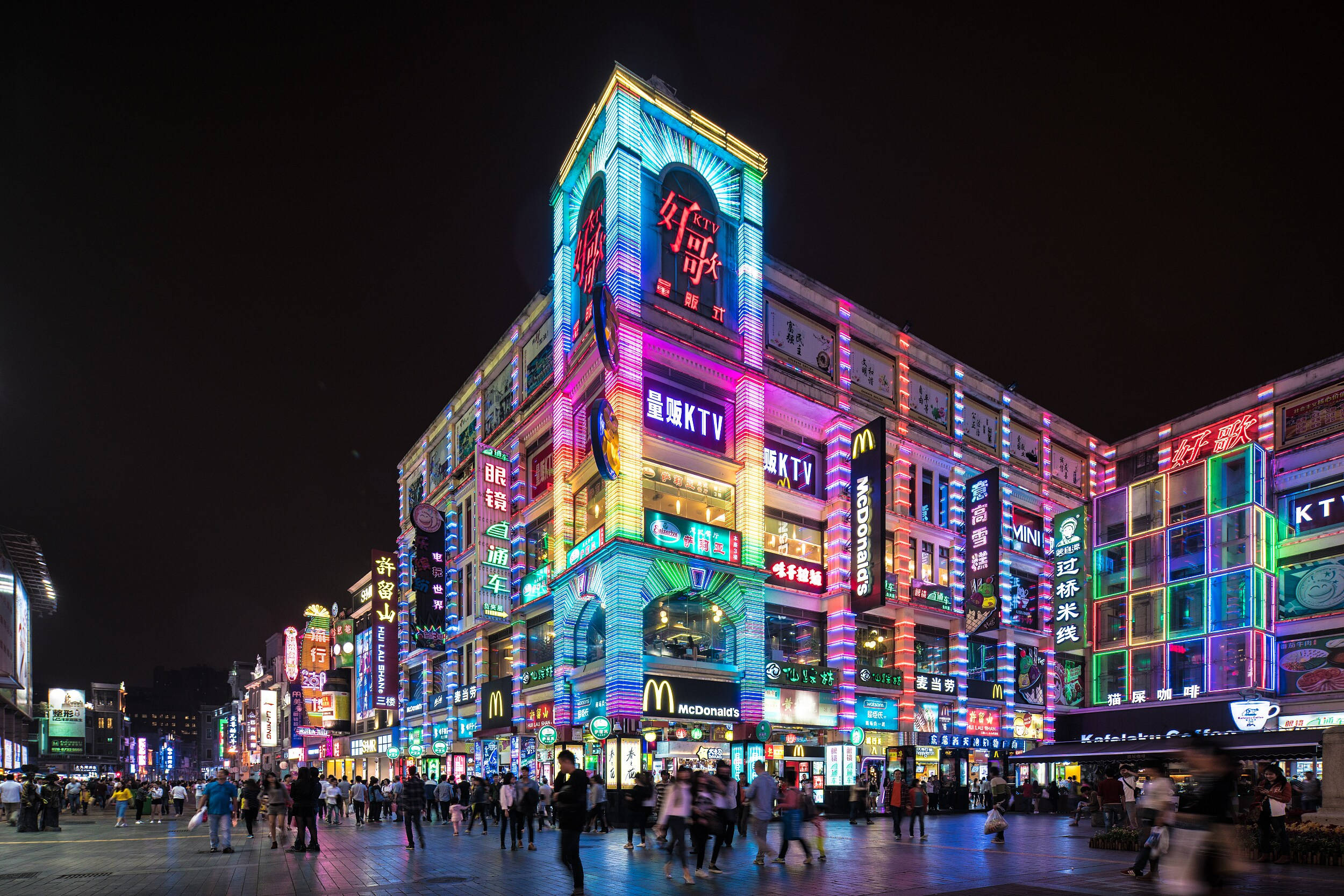 Guangzhou 桌布 壁紙 — 繁華都市街道的耀眼夜景，兩旁是明亮照明的霓虹招牌和高聳的商業建築。