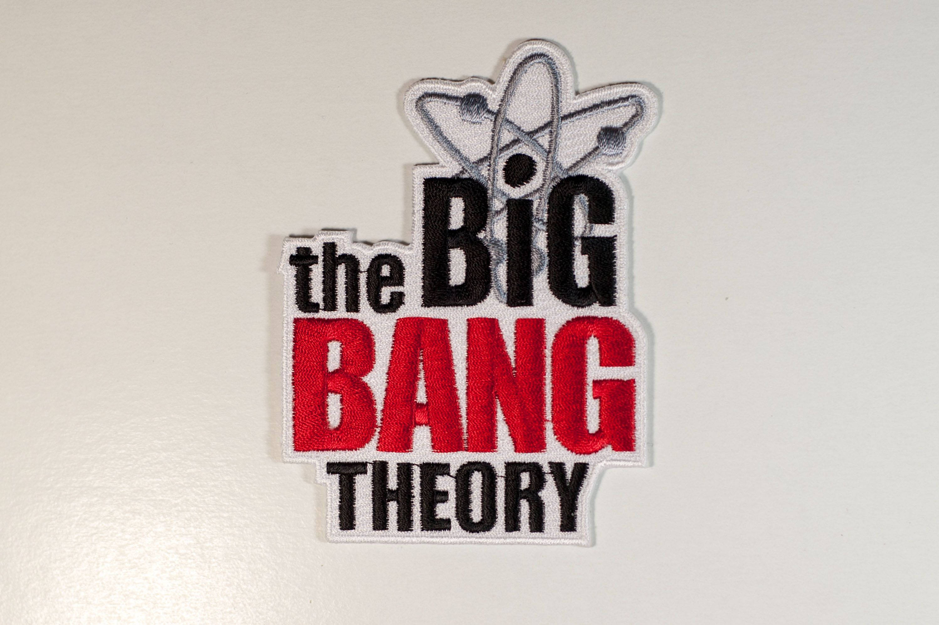 Bang 桌布 壁紙 — 繡有 'The Big Bang Theory' 的補丁，帶有紅色、黑色和銀色文字及原子符號，背景為純白色。