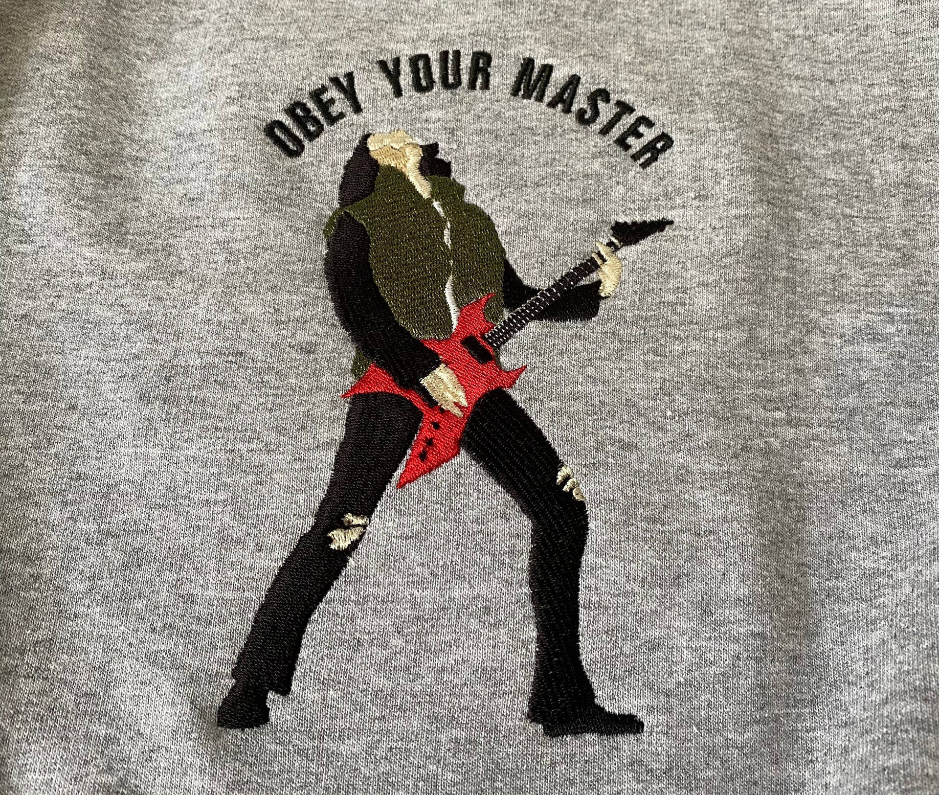 繡有龐克搖滾者彈奏紅色吉他，並帶有'OBEY YOUR MASTER'文字，位於灰色衛衣上。 — 吉他動圖 壁紙