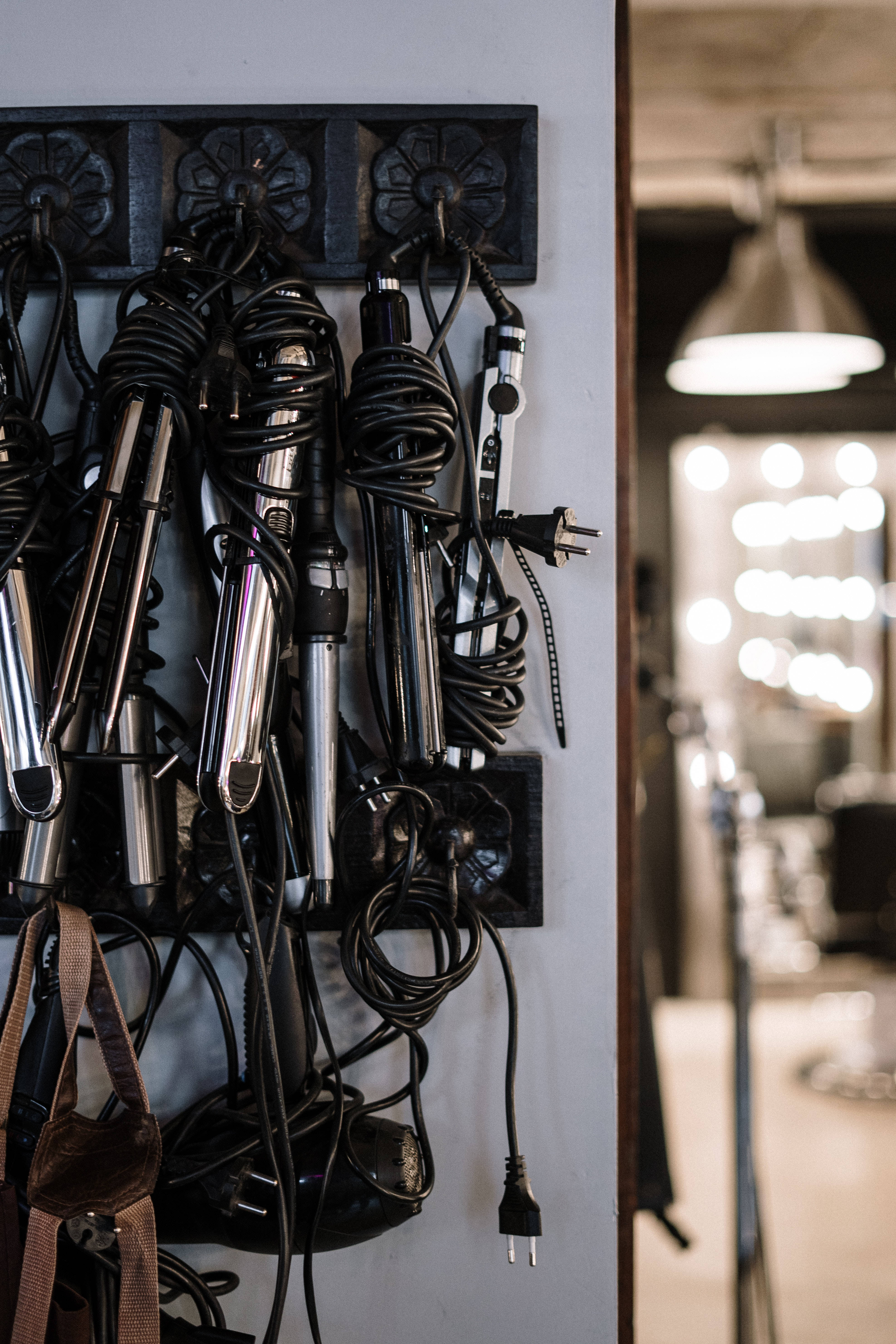 Salon 桌布 壁紙 — 纏結的黑色電線和鉻色美髮工具整齊地掛在溫暖照明的沙龍牆架上。