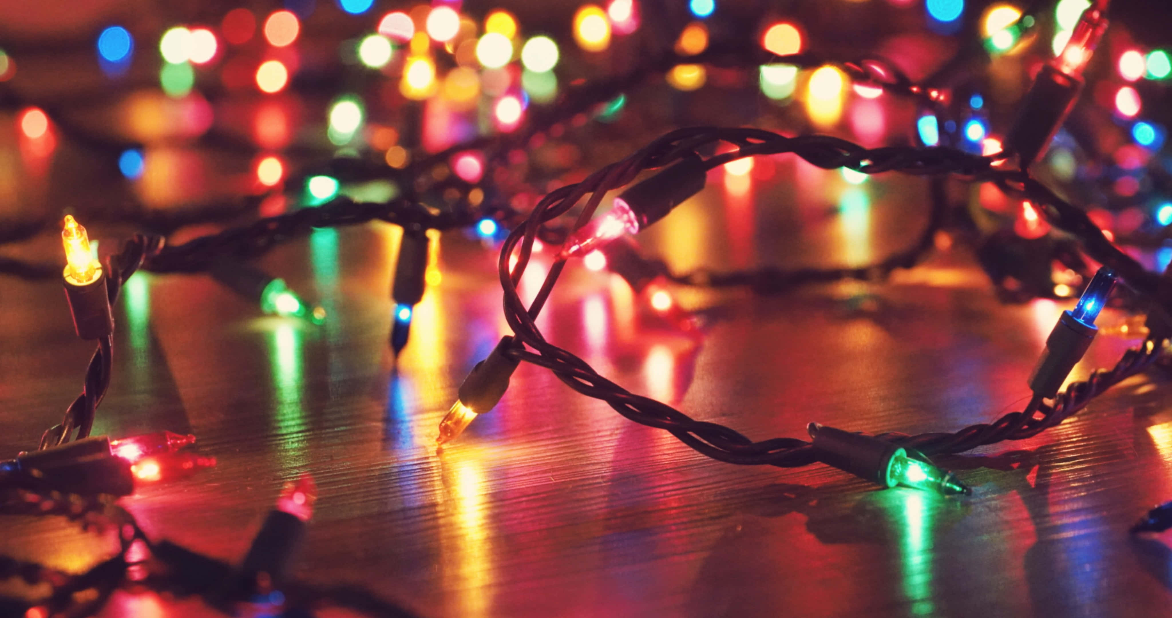 Christmas Light 桌布 壁紙 — 纏繞的燈串在木質表面上溫暖地發光，背景有色彩繽紛的散景。