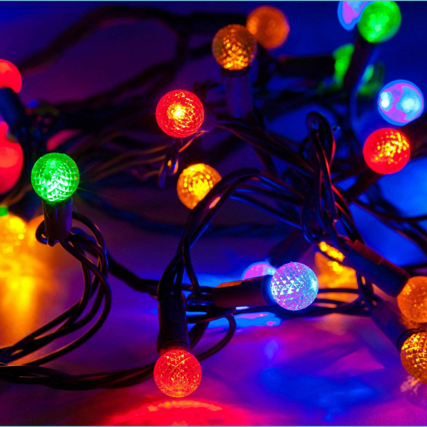Christmas Lights Aesthetic 桌布 壁紙 — 纏繞的發光迪斯科球燈串，有紅色、綠色、藍色和橙色，背景為深色。