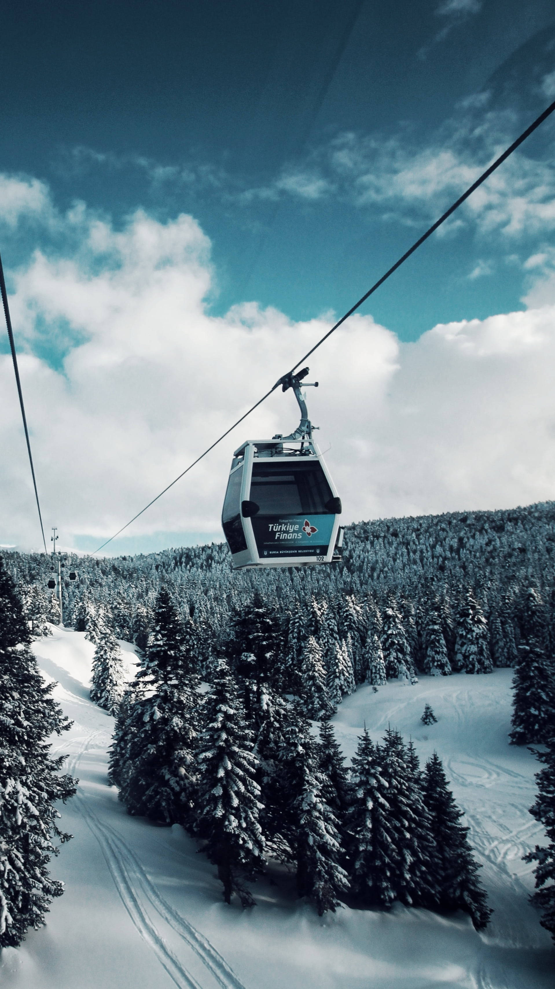 雲朵 桌布 壁紙 — 纜車在部分多雲的天空下滑過白雪覆蓋的森林山坡。