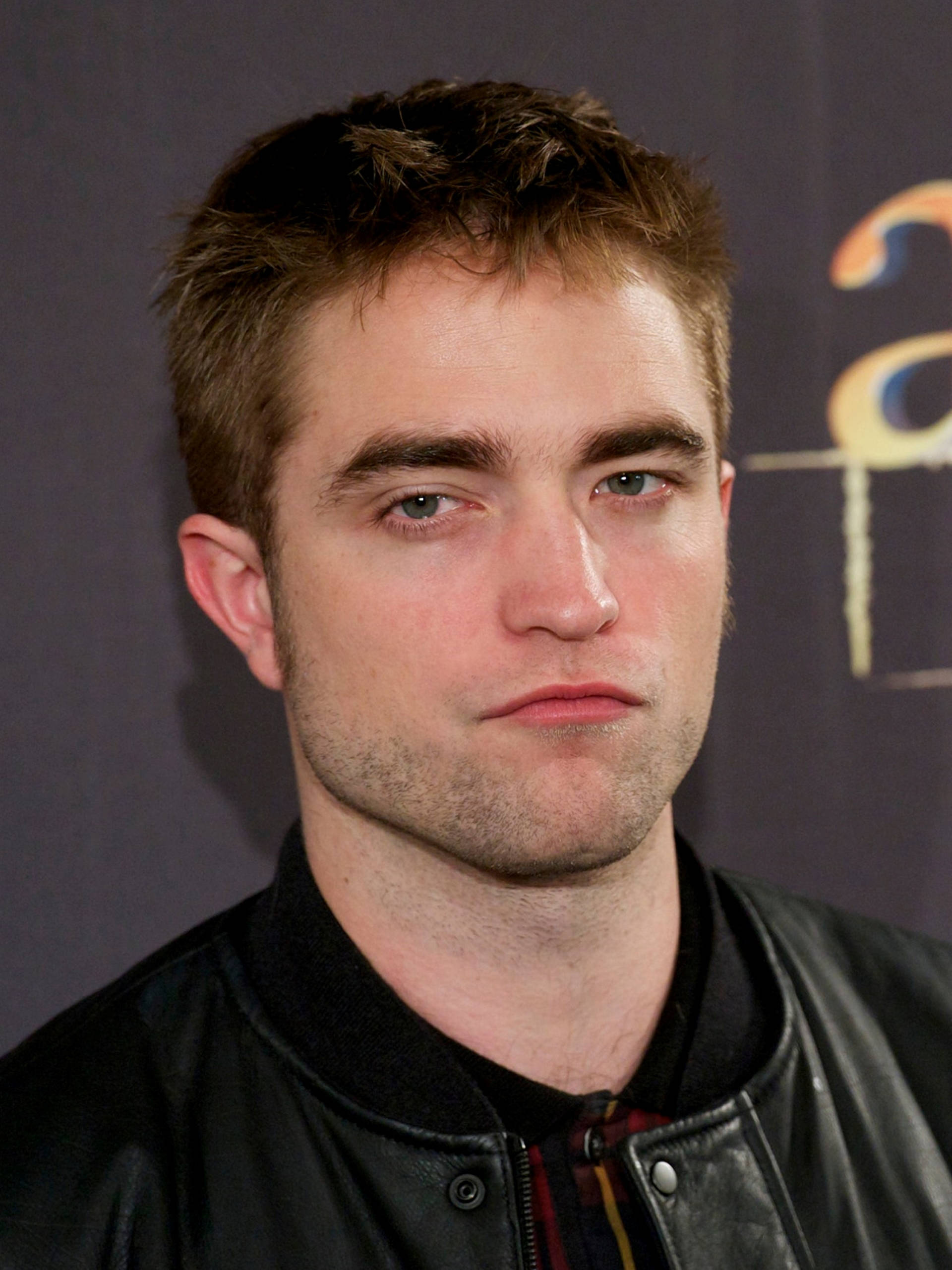 Robert Pattinson 桌布 壁紙 — 羅伯·派汀森在特寫肖像中凝視，穿著黑色皮夾克，背景昏暗。