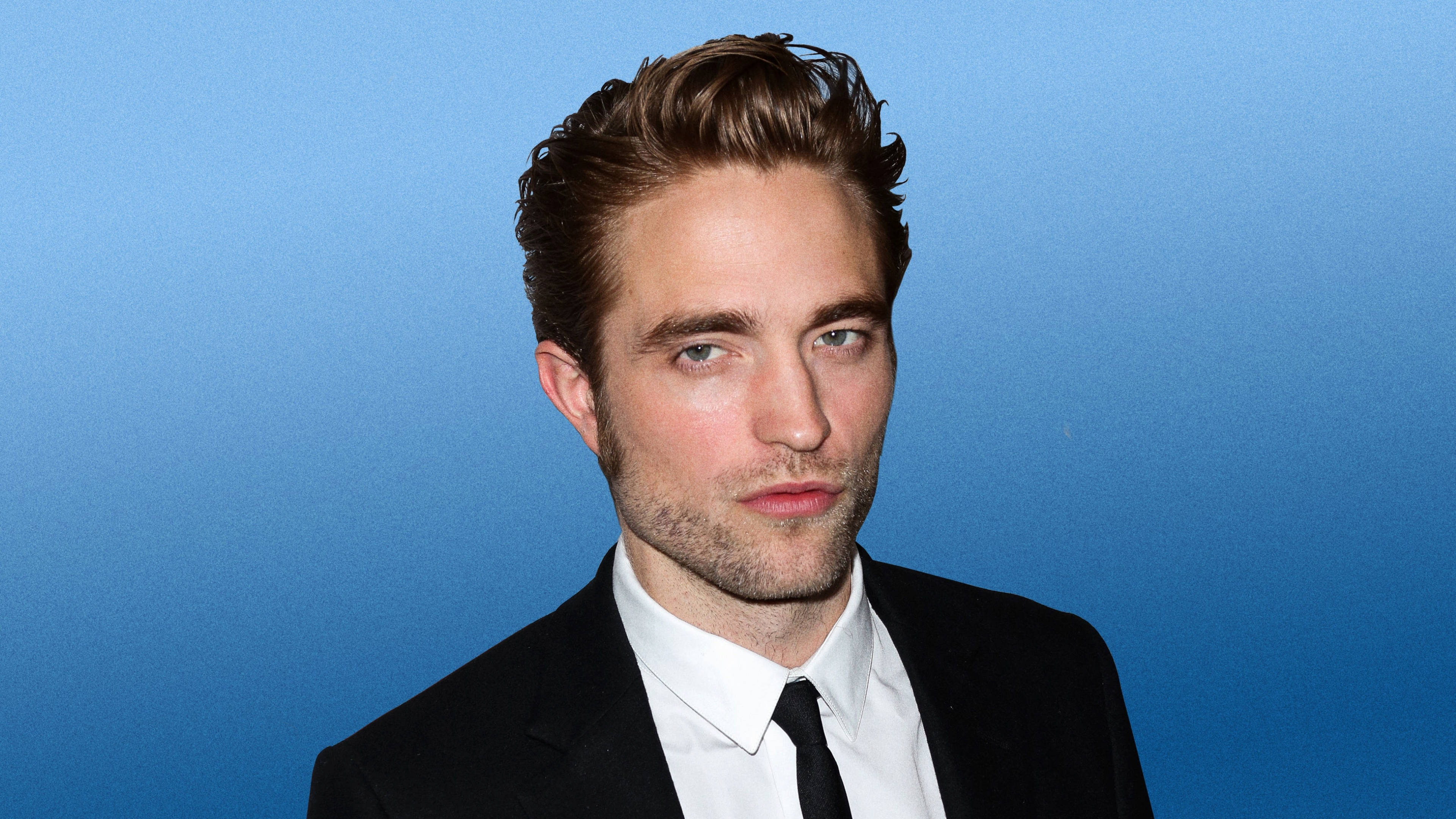 Robert Pattinson 桌布 壁紙 — 羅伯·派汀森身穿俐落黑色西裝和領帶，在純藍色攝影棚背景前，直接打光。