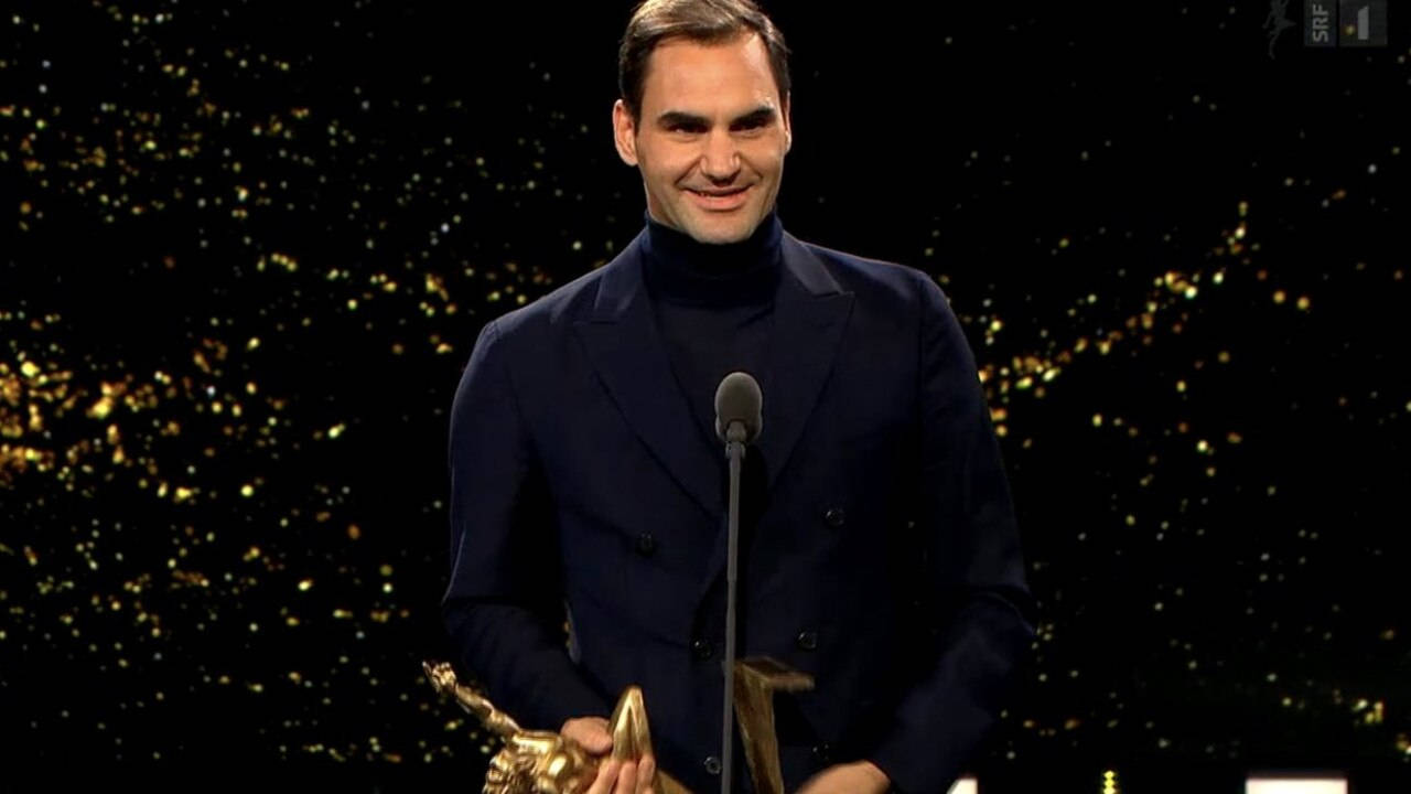 roger 桌布 壁紙 — 羅傑·費德勒在明亮的燈光下，於閃爍的舞台上溫暖地微笑，手持金色獎盃。