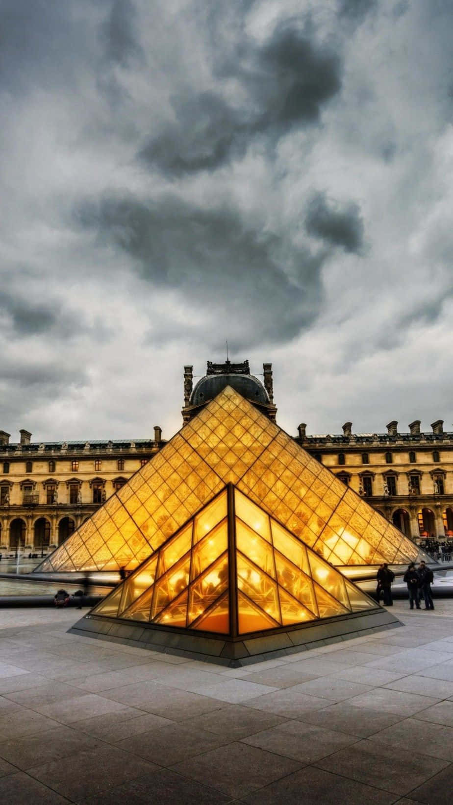 pyramid 桌布 壁紙 — 羅浮宮博物館閃閃發光的玻璃金字塔在黃昏時分戲劇性的多雲天空下閃耀。