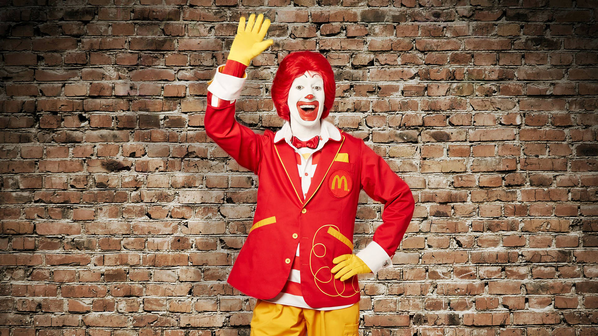 Mcdonalds 桌布 壁紙 — 羅納德·麥當勞穿著經典紅黃色西裝，在風化的磚牆背景下愉快地揮手。