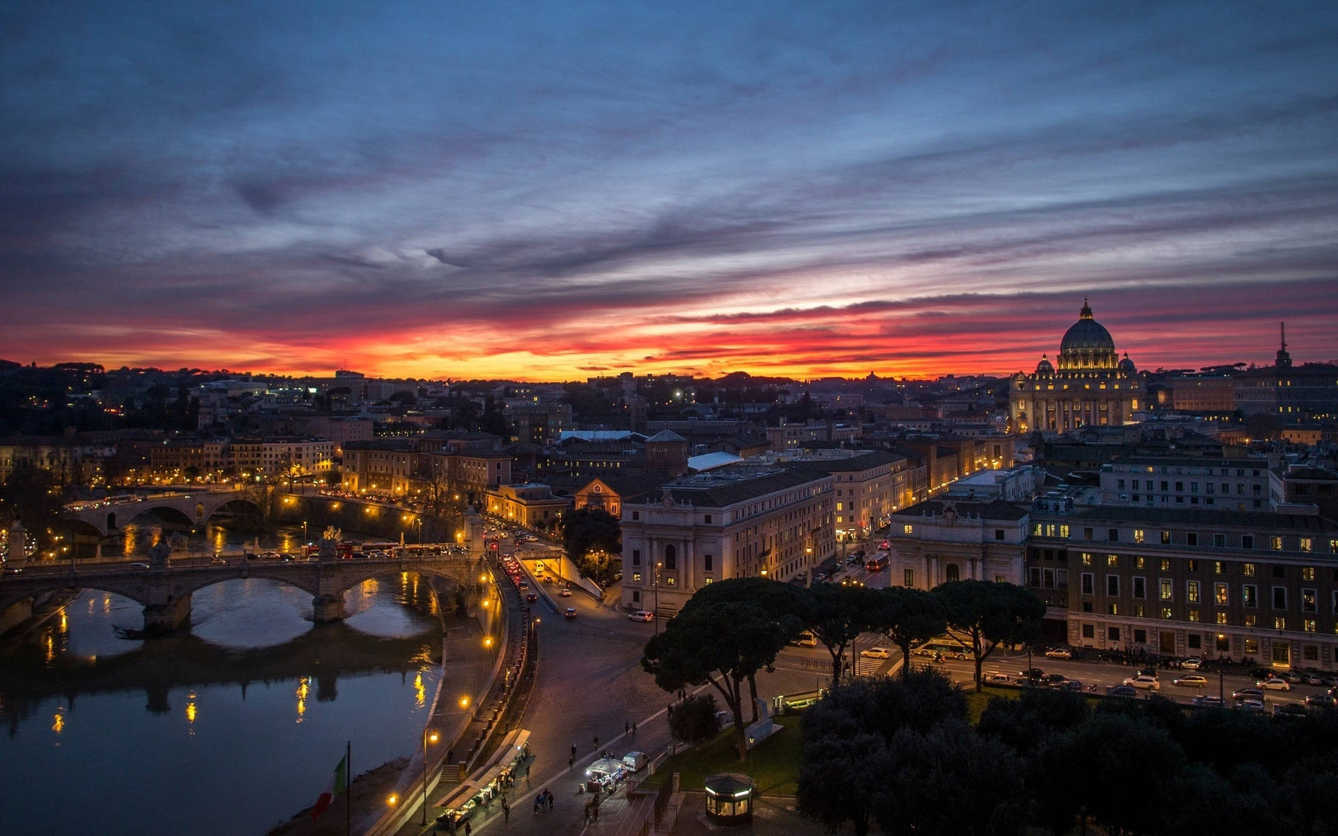 Rome 桌布 壁紙 — 羅馬令人驚嘆的日落，聖彼得大教堂在台伯河和歷史橋樑上方火熱的橙色和紫色雲彩中閃耀。