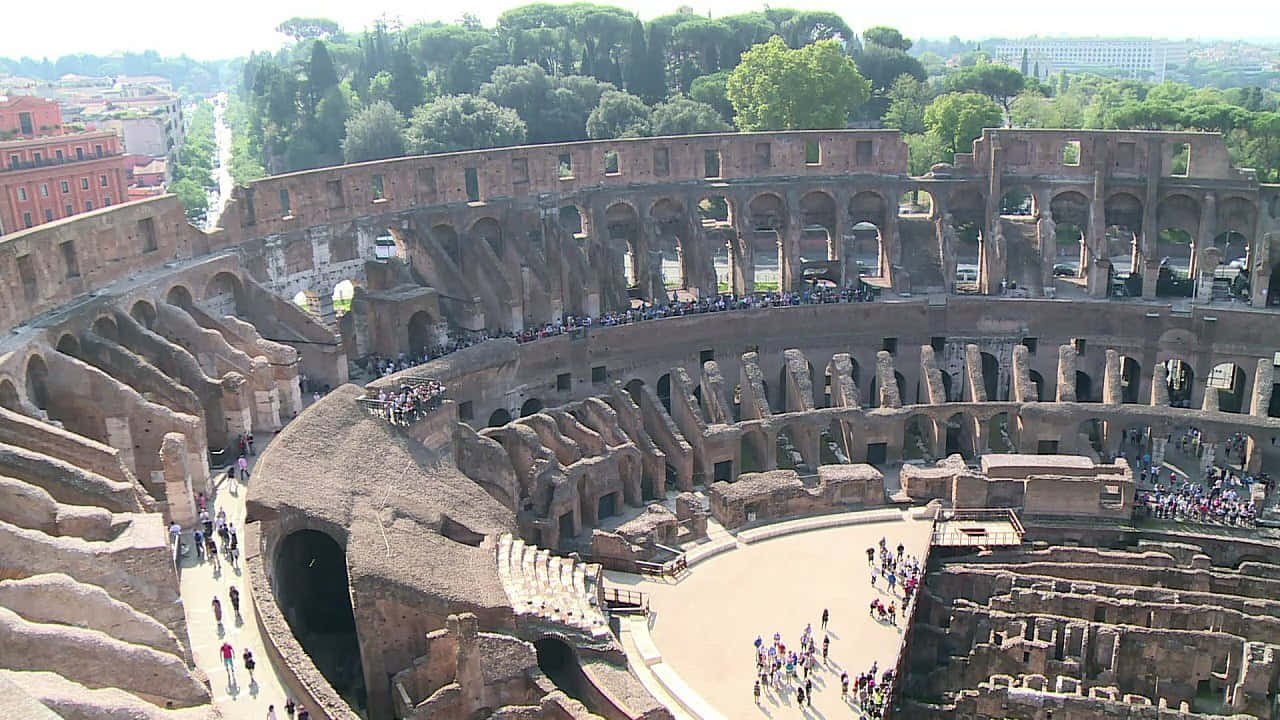 Roman Colosseum 桌布 壁紙 — 羅馬古羅馬競技場的鳥瞰圖，遊客在明亮的日光下探索其巨大的石頭廢墟。