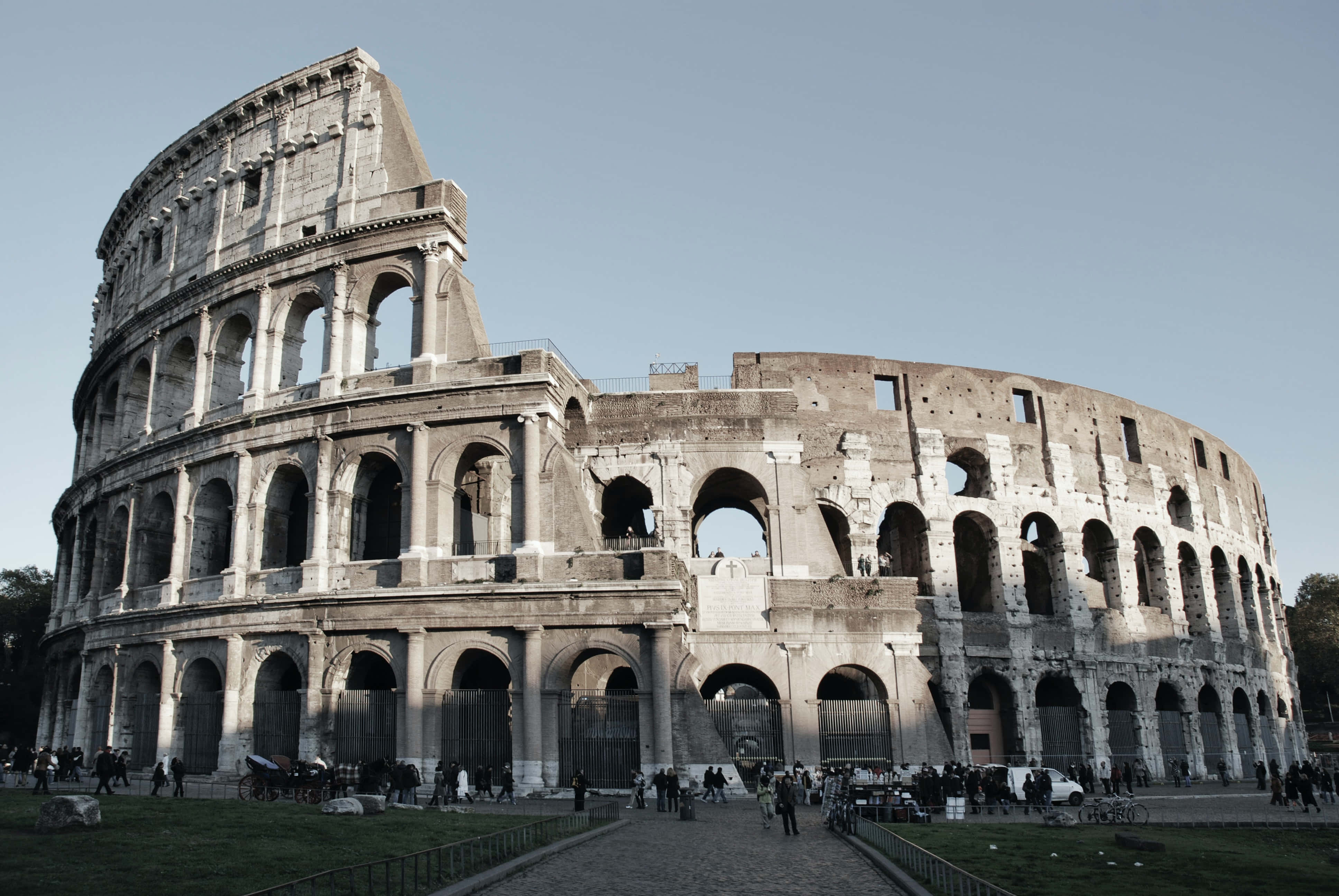 Ancient Roman Desktop 桌布 壁紙 — 羅馬的古代競技場在晴朗的天空下雄偉地矗立，遊客正在探索其歷史遺跡。