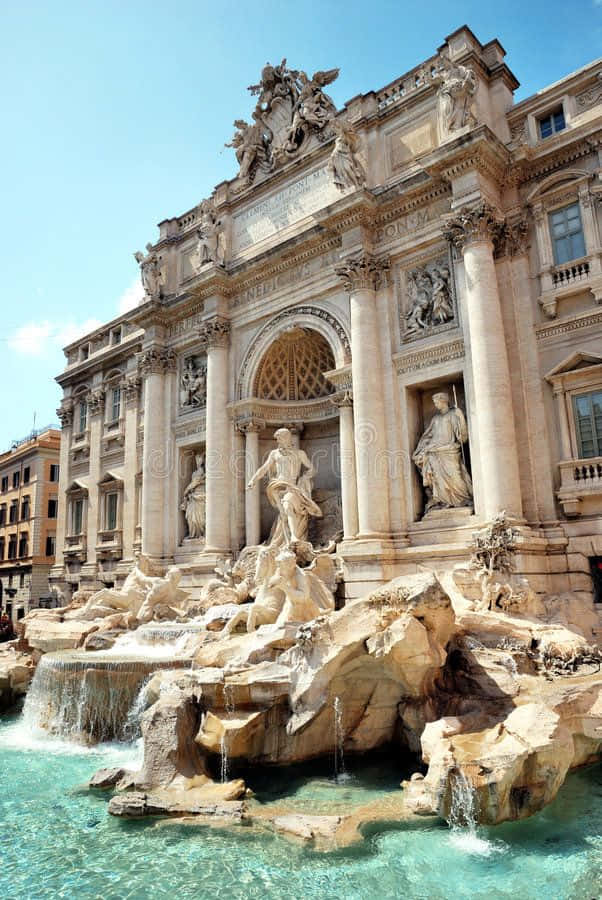 Rome 桌布 壁紙 — 羅馬的特雷維噴泉在明亮的藍天下流淌著清澈的藍綠色水，其宏偉的巴洛克式建築裝飾著大理石雕像和柱子。