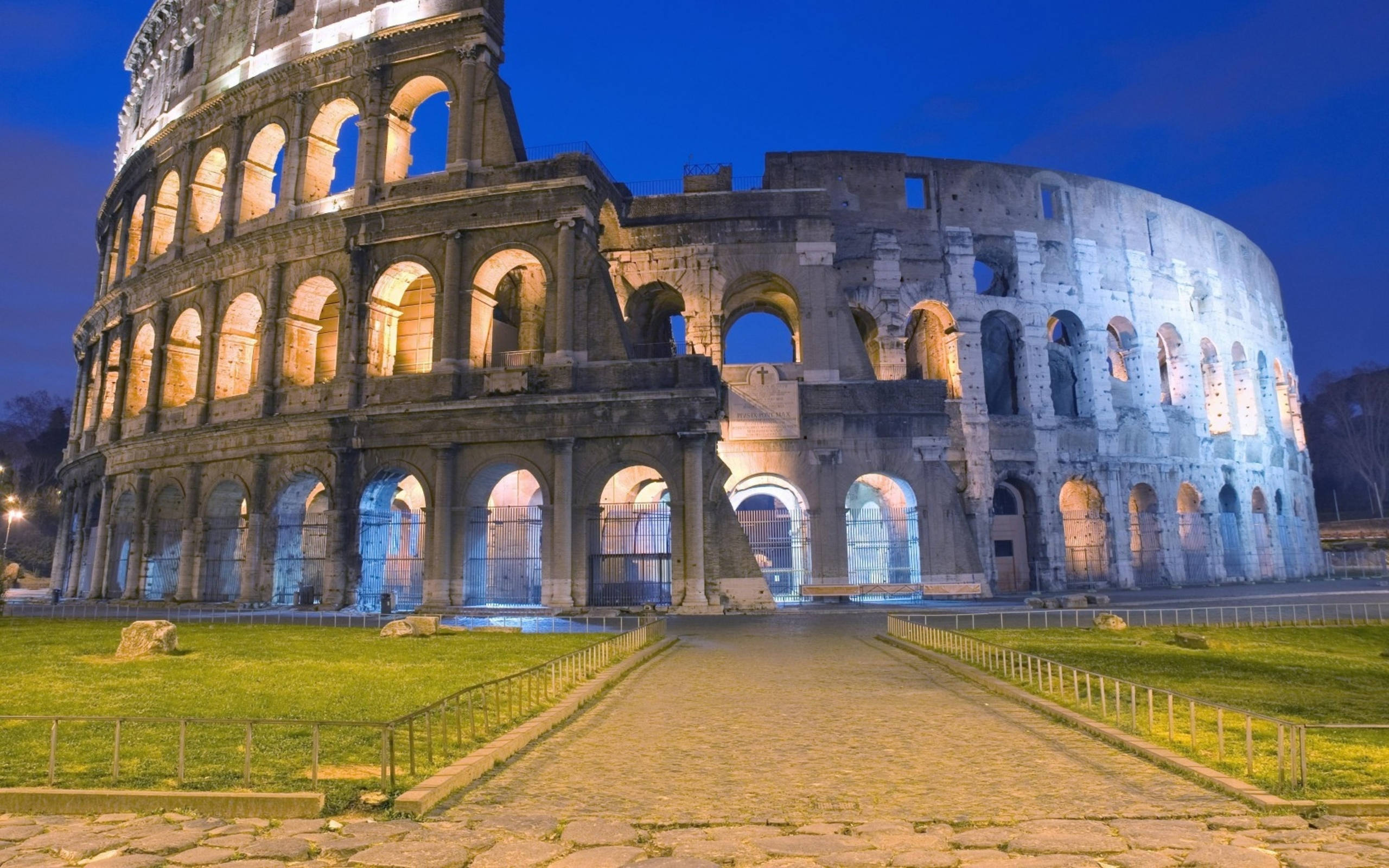Rome 桌布 壁紙 — 羅馬競技場在傍晚燈光下溫暖地發光，襯托著深藍色的暮色天空。