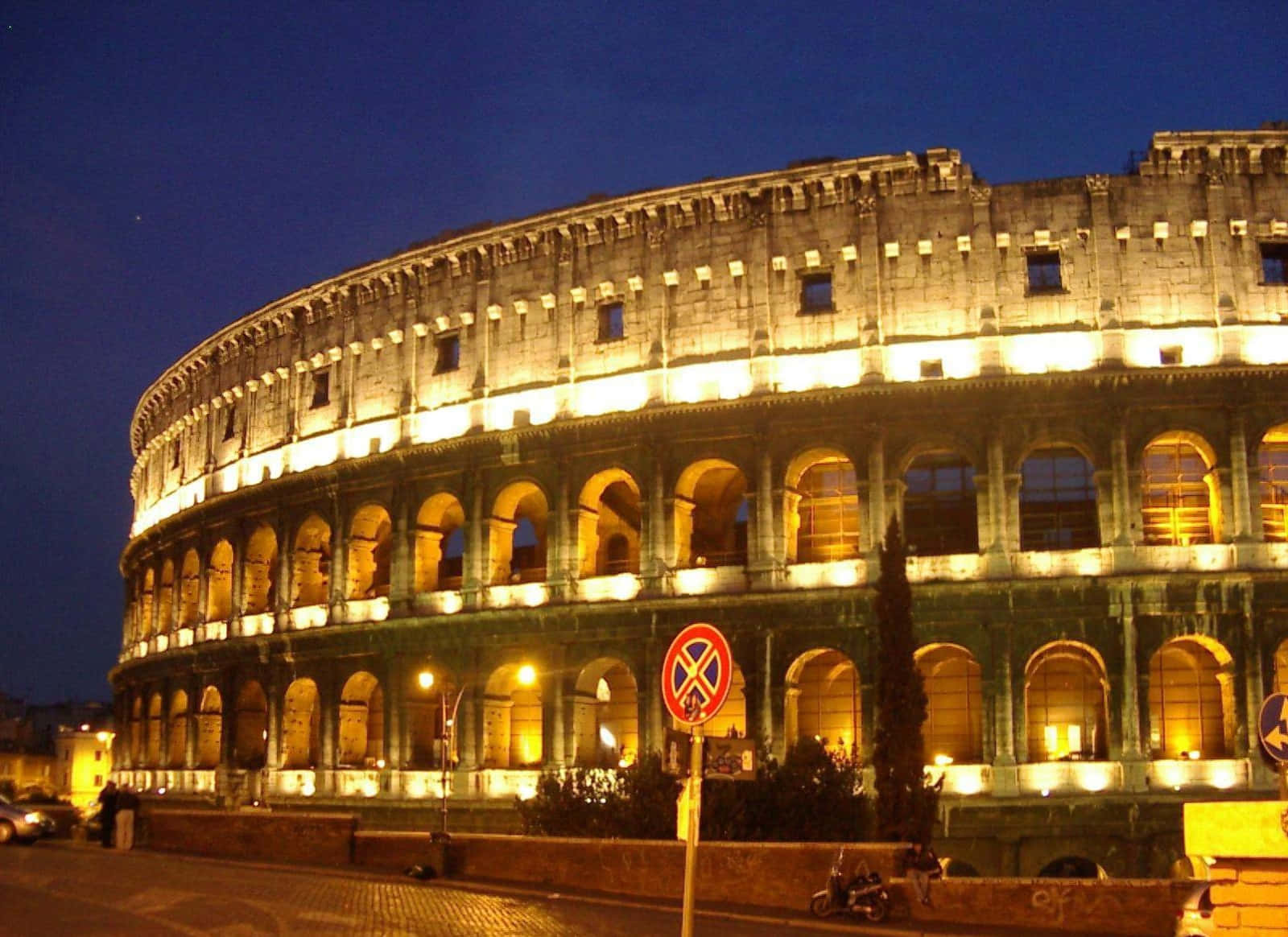 Roman 桌布 壁紙 — 羅馬競技場在夜晚燈光下溫暖地發光，襯托著深藍色的暮色天空。