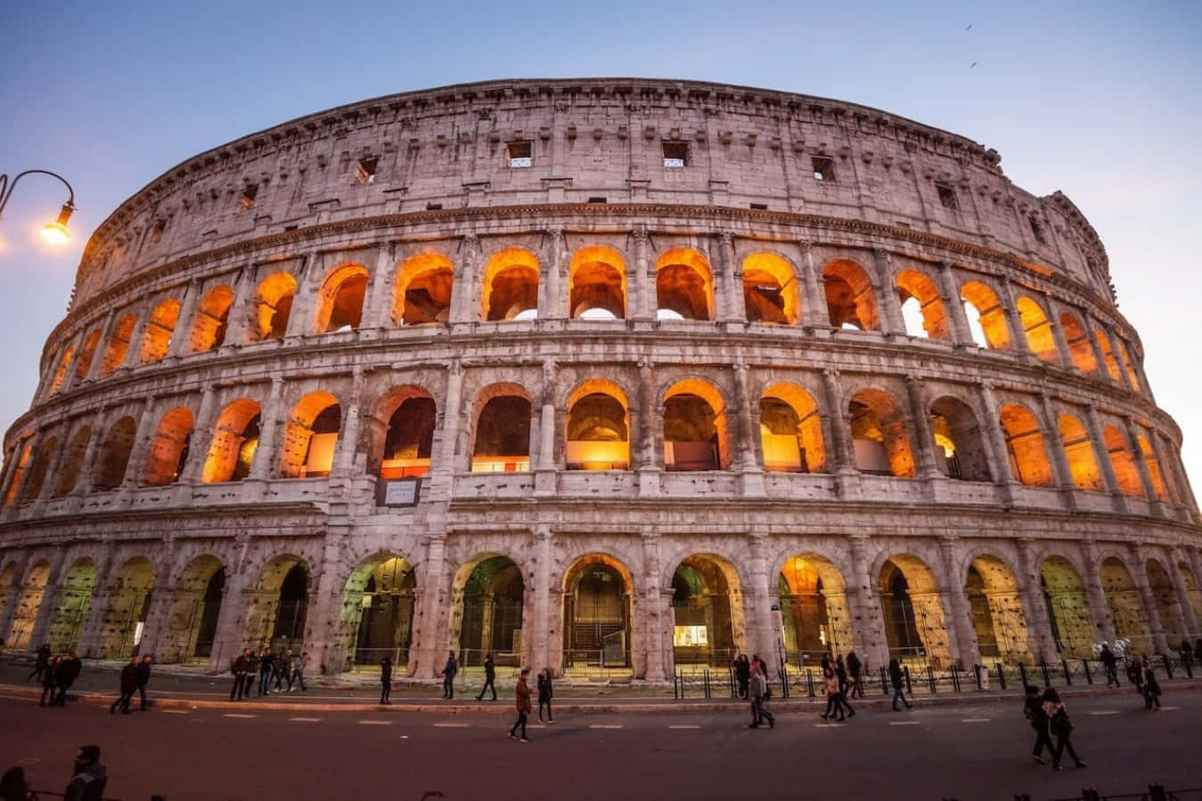 Roman 桌布 壁紙 — 羅馬競技場在黃昏時溫暖地發光，遊客在其古老的拱門下漫步。