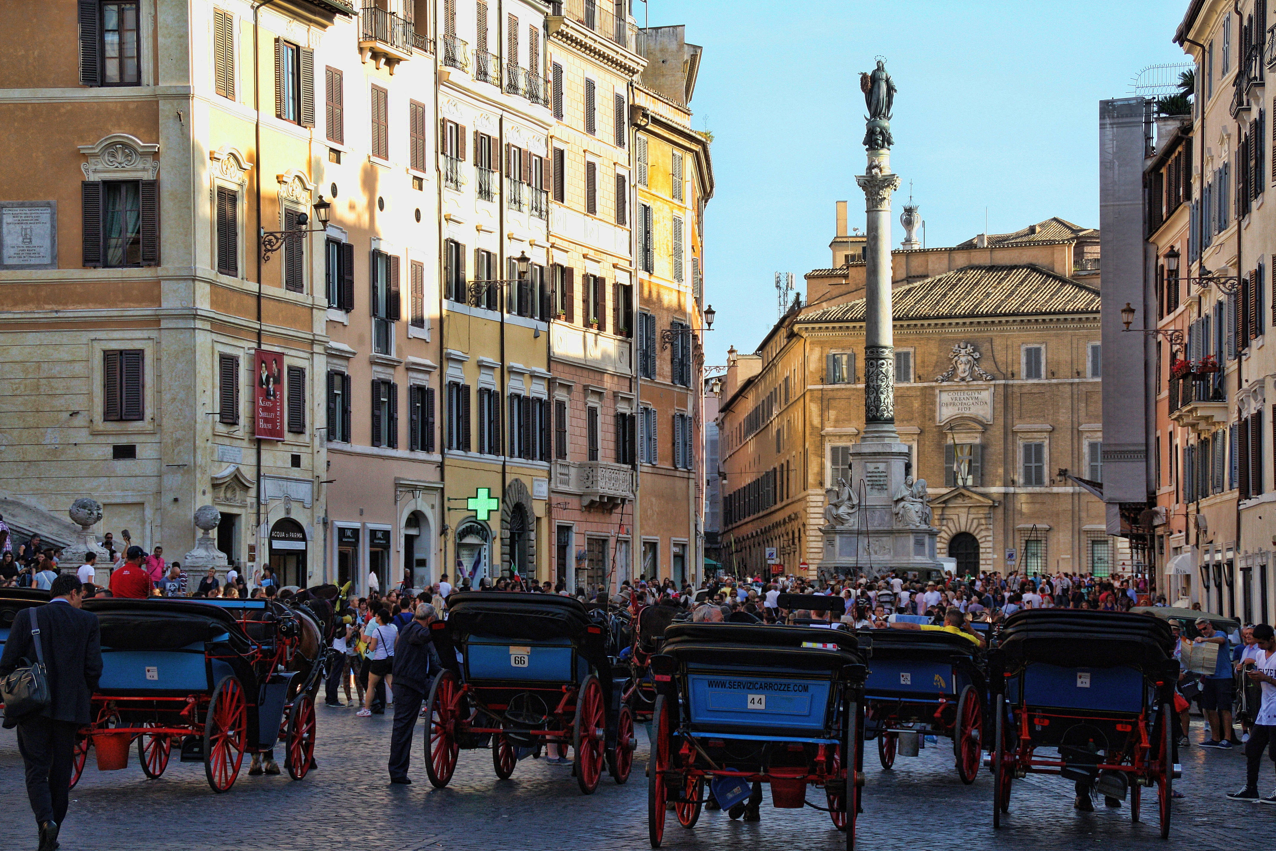 Rome 桌布 壁紙 — 羅馬陽光普照的鵝卵石街道，附近有高大的圓柱紀念碑，擠滿了馬車和遊客。