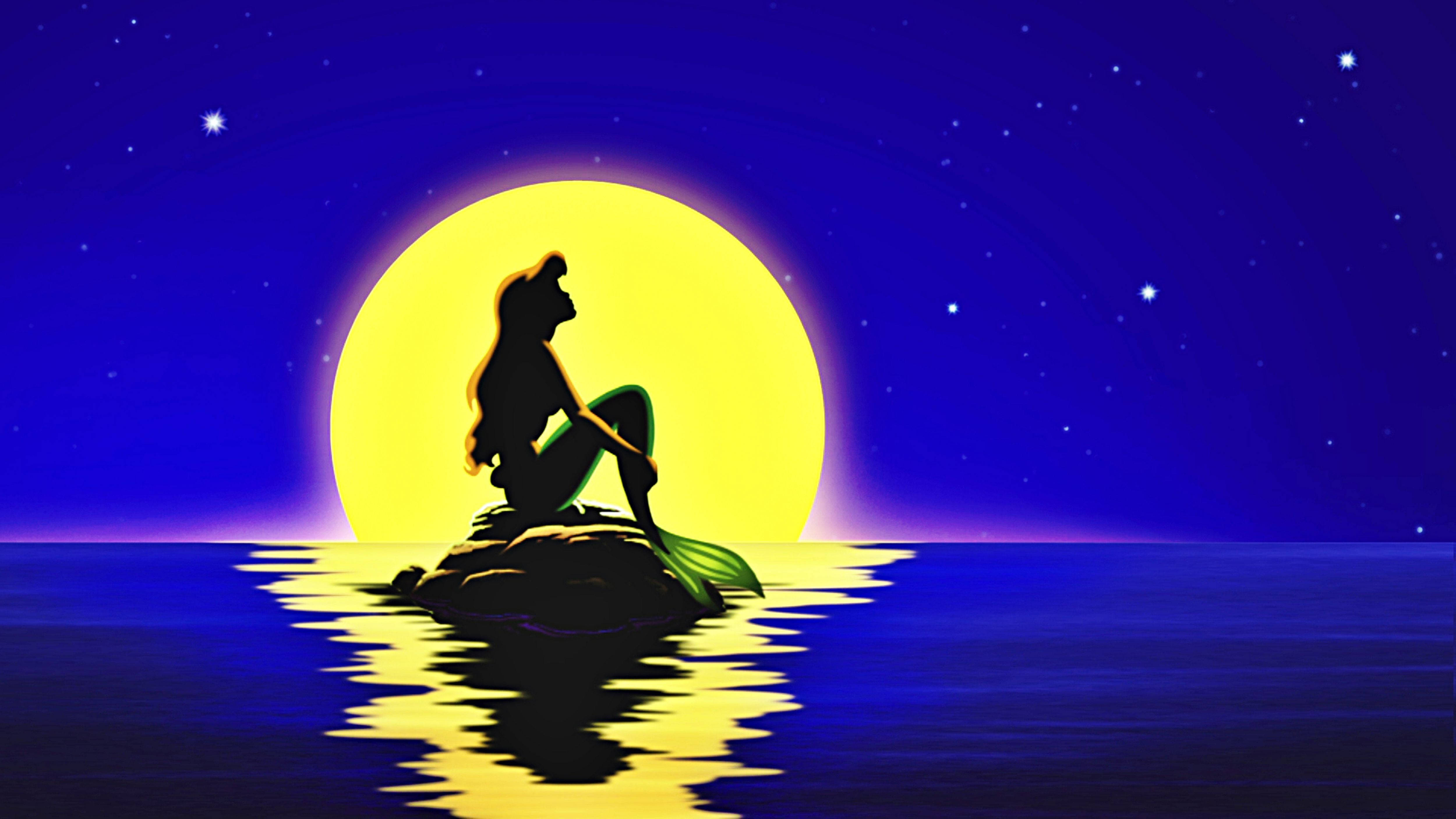 迪士尼公主 桌布 壁紙 — 美人魚剪影坐在岩石上，凝視著夜空中星羅棋布的海洋上方一輪巨大的發光月亮。