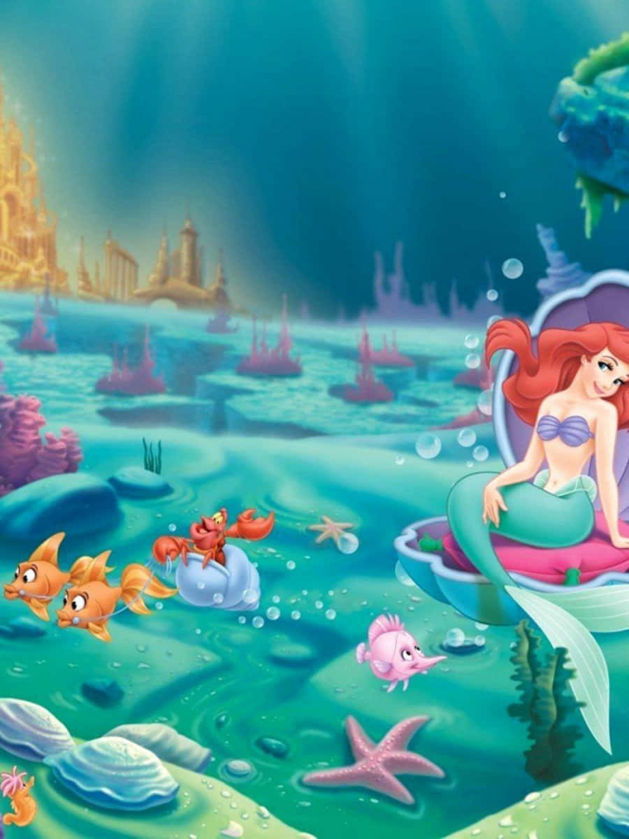 Kawaii Mermaid 桌布 壁紙 — 美人魚艾莉兒坐在水中的貝殼寶座上，與她的朋友們（包括小比目魚和賽巴斯丁）一起，附近有陽光照射的珊瑚礁和遠處的城堡。