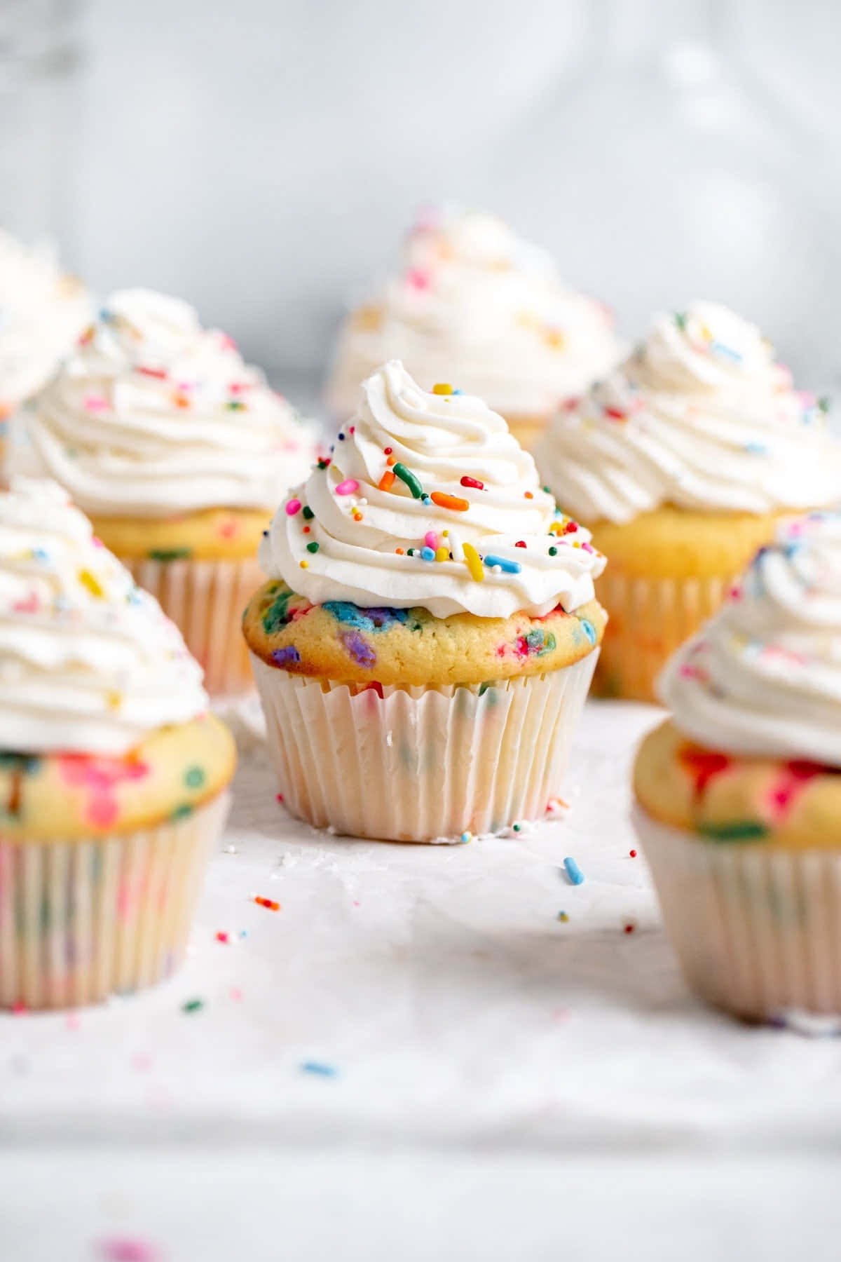 Cupcake 桌布 壁紙 — 美味的funfetti杯子蛋糕，上面有彩虹糖針和蓬鬆白色糖霜，擺放在大理石檯面上。