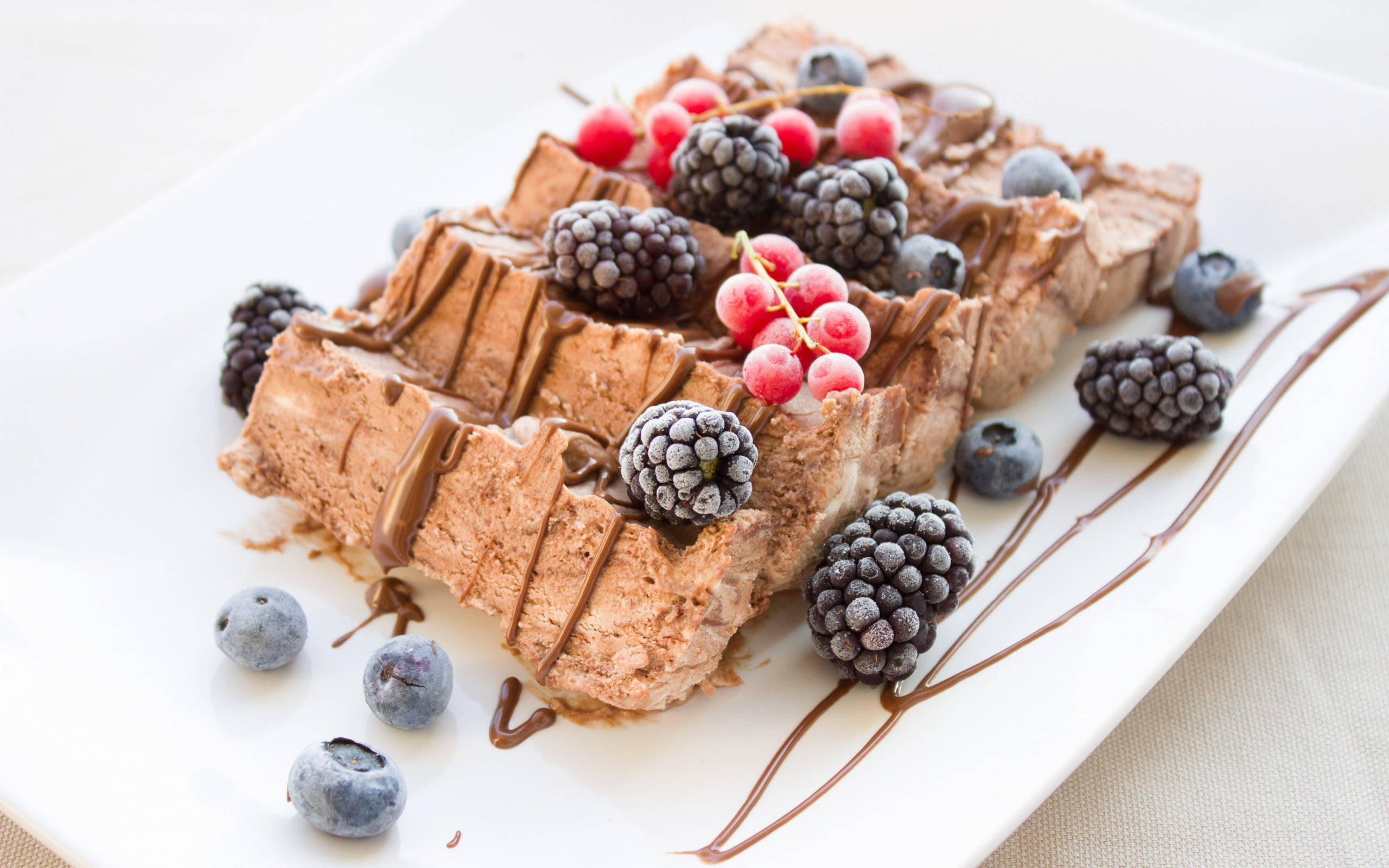 Waffle 桌布 壁紙 — 美味的巧克力慕斯甜點切片，上面放上新鮮莓果並淋上巧克力醬，擺在白色盤子上。