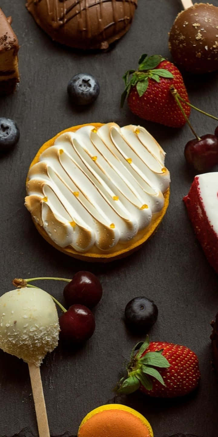 Pastry 桌布 壁紙 — 美味的甜點組合，包括蛋白霜塔、草莓、櫻桃和巧克力點心，擺放在深色石板表面上。