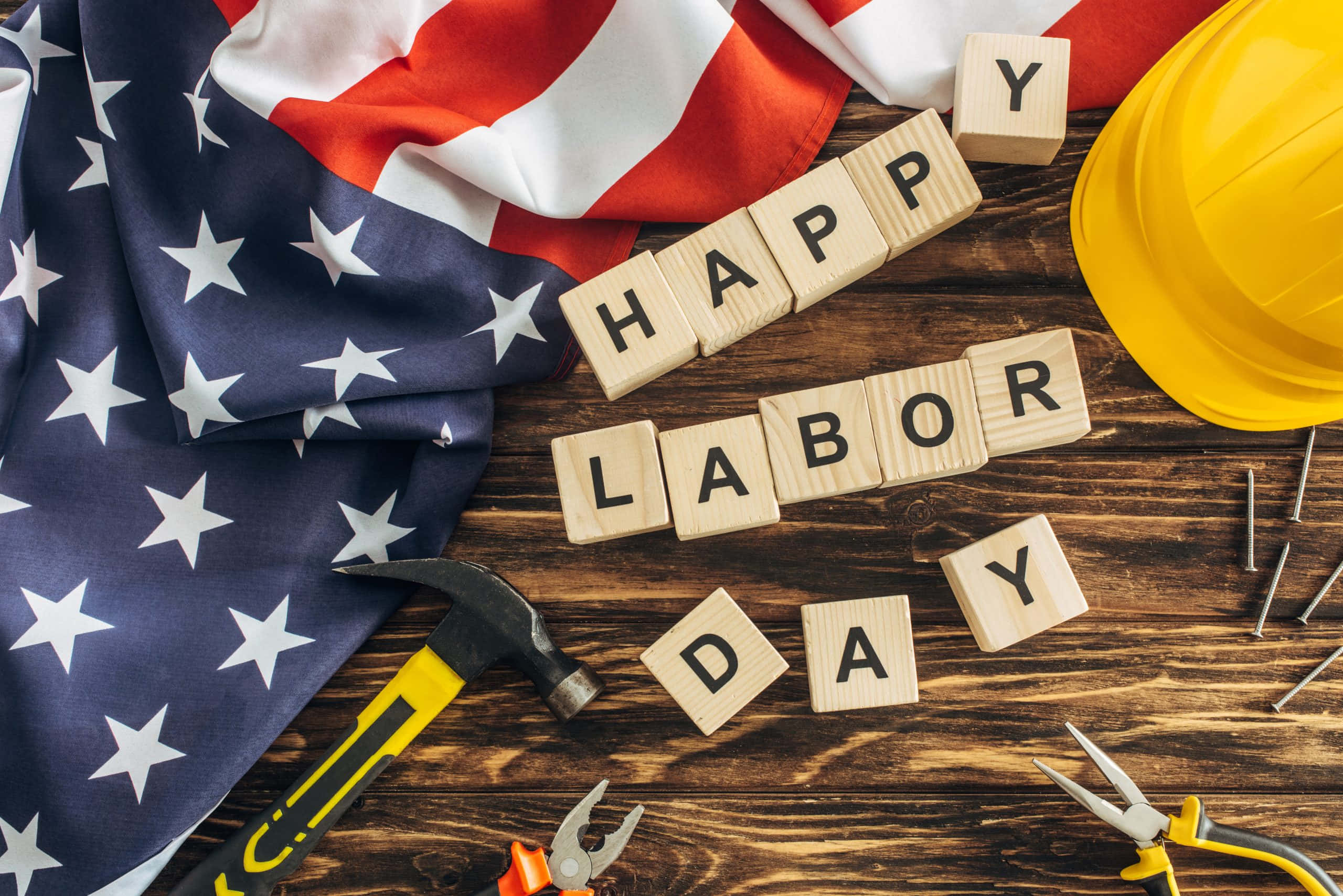 勞動節 桌布 壁紙 — 美國國旗和建築工具圍繞著在質樸工作台上拼出「HAPPY LABOR DAY」的木塊。