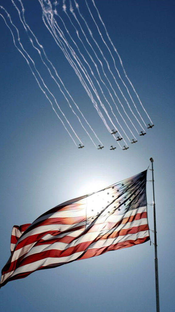 American Flag iPhone 桌布 壁紙 — 美國國旗在噴射機編隊下方自豪地飄揚，噴射機在清澈的藍天上留下白色煙跡。