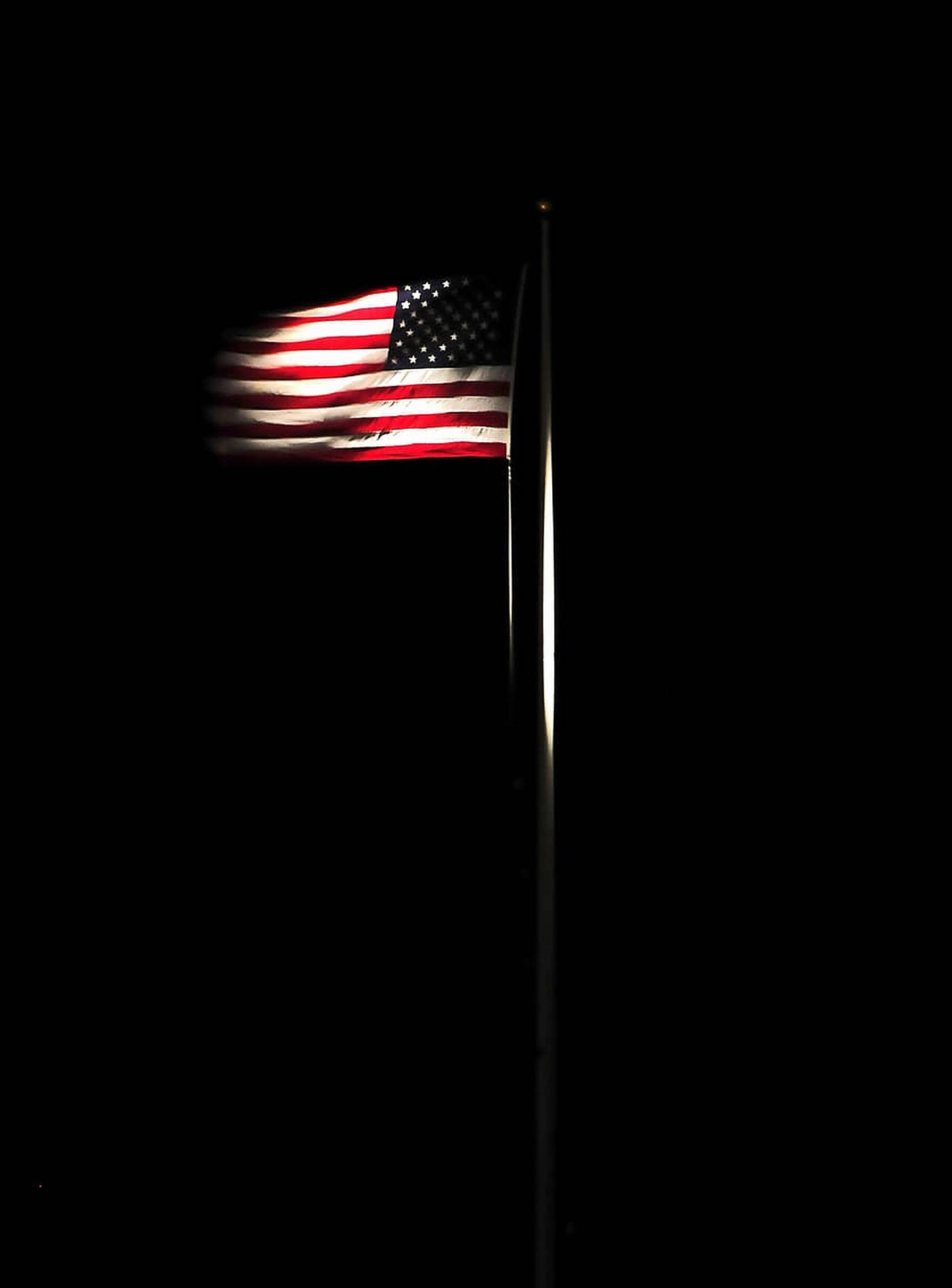 Black American Flag 桌布 壁紙 — 美國國旗在夜間照亮，背景是漆黑的天空，帶有微妙的動態模糊效果。