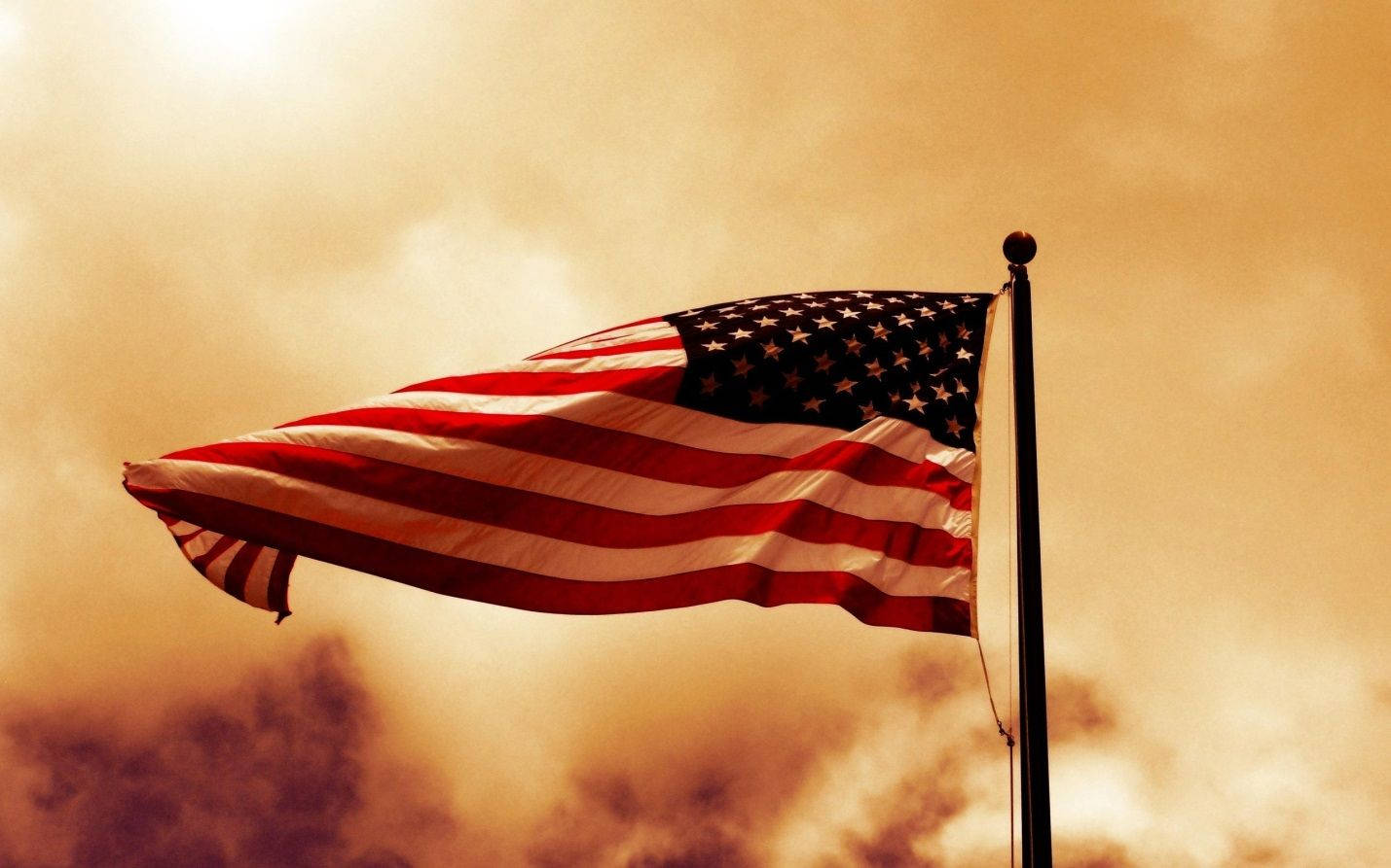 American 桌布 壁紙 — 美國國旗在戲劇性的金色日落天空和翻滾的雲彩中自豪地飄揚。