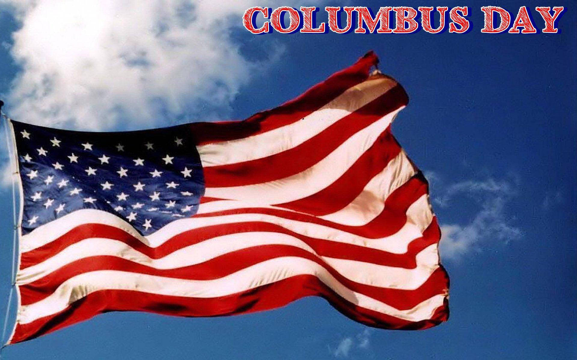 Columbus Day 桌布 壁紙 — 美國國旗在明亮的藍天、蓬鬆的白雲和粗體紅色文字「哥倫布日」中自豪地飄揚。