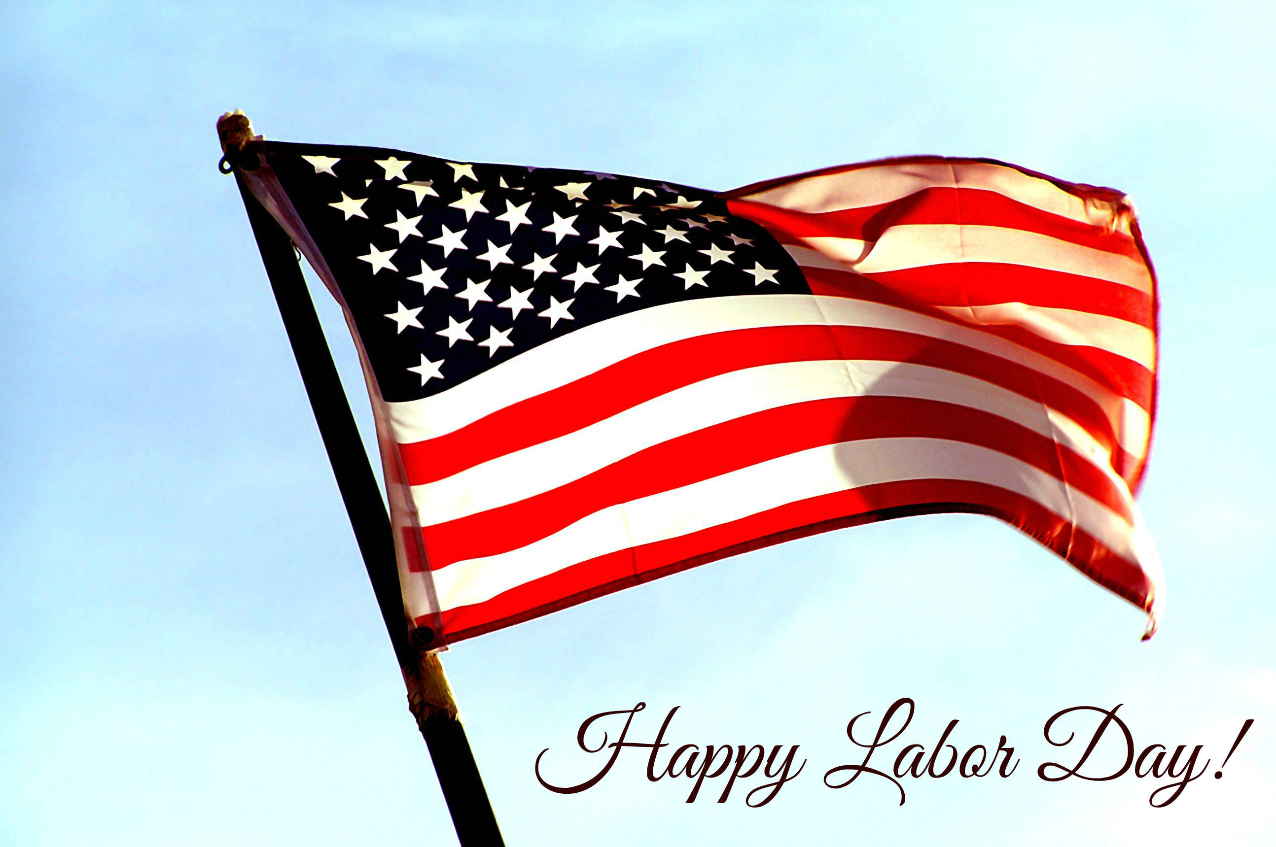 Labor 桌布 壁紙 — 美國國旗在晴朗的藍天下自豪地飄揚，下方寫有「Happy Labor Day!」。