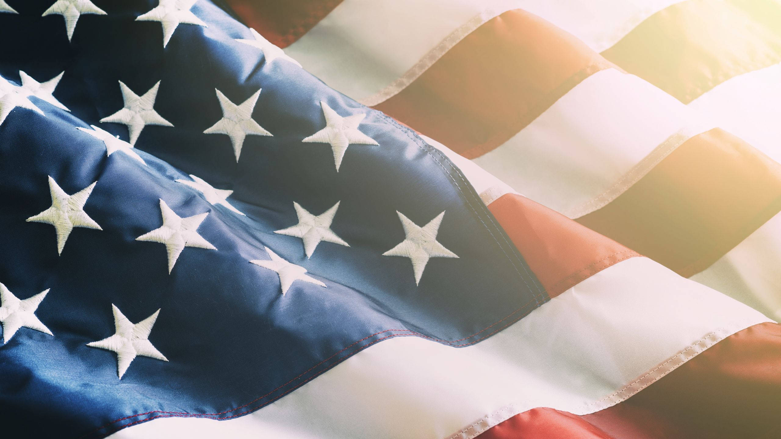 Veterans 桌布 壁紙 — 美國國旗在溫暖陽光下飄揚，星星和條紋在特寫細節中波動。