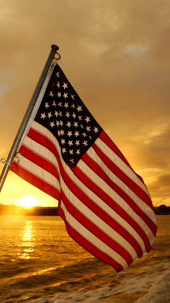 American Flag iPhone 桌布 壁紙 — 美國國旗在金色日落映照下，在水面上自豪地飄揚，陽光在水波上反射。