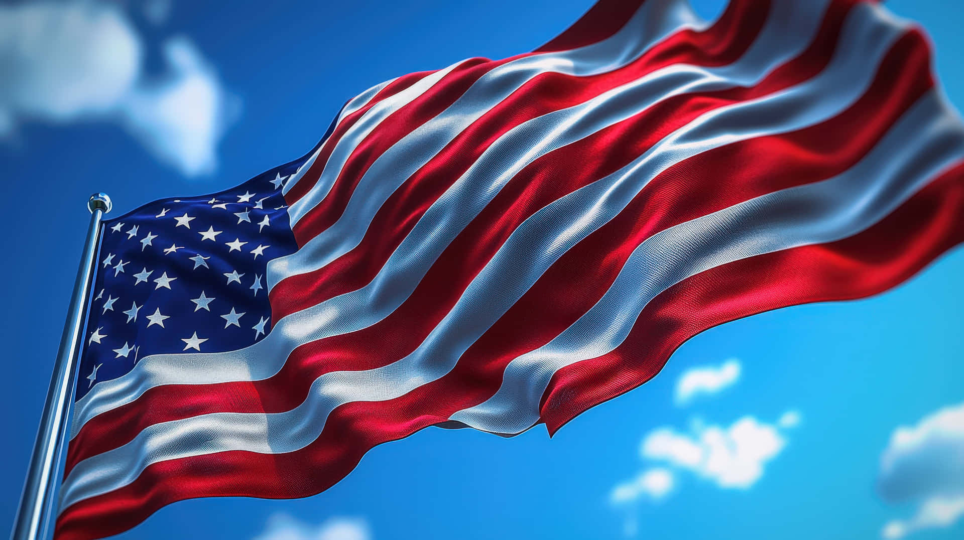 American flag waving in the wind against a bright blue sky 壁紙 — 美國國旗帶有紅白條紋和藍色星域，在明亮的藍天和散落的雲朵中動態飄揚。