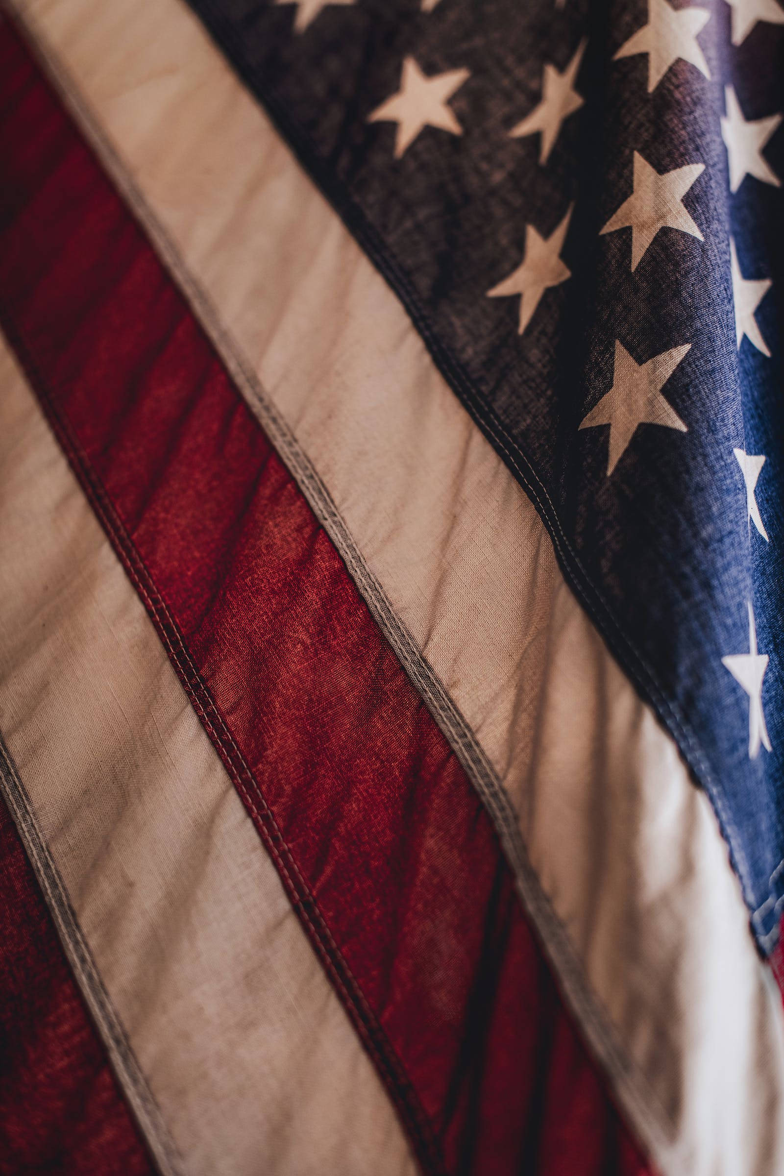 American Flag iPhone 桌布 壁紙 — 美國國旗特寫，帶有紅色、白色和藍色條紋和星星，顯示布料質地和褶皺，呈現風化痕跡。