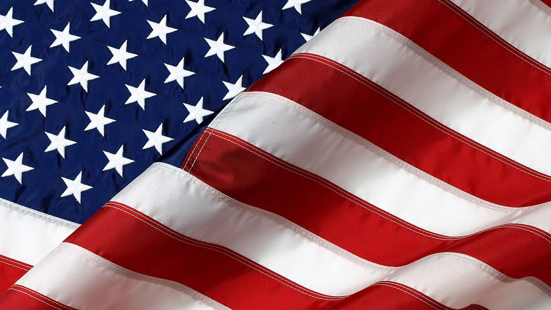 American 桌布 壁紙 — 美國國旗近距離特寫，旗幟飄揚，紅白藍條紋和星星展現布料質感和摺痕。