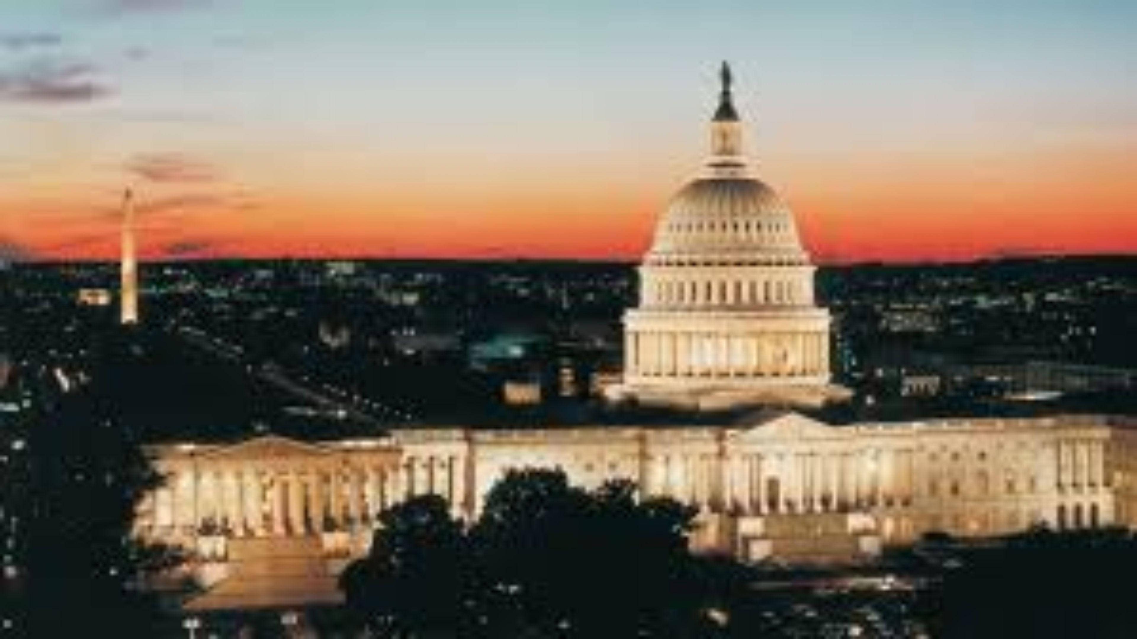 Washington 桌布 壁紙 — 美國國會大廈在充滿活力的橙色和藍色日落天空下溫暖地發光，下方城市燈光閃爍。