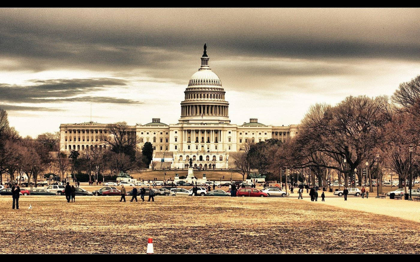 Washington 桌布 壁紙 — 美國國會大廈在戲劇性的陰天下莊嚴聳立，周圍有光禿的樹木和人們在草坪上行走。