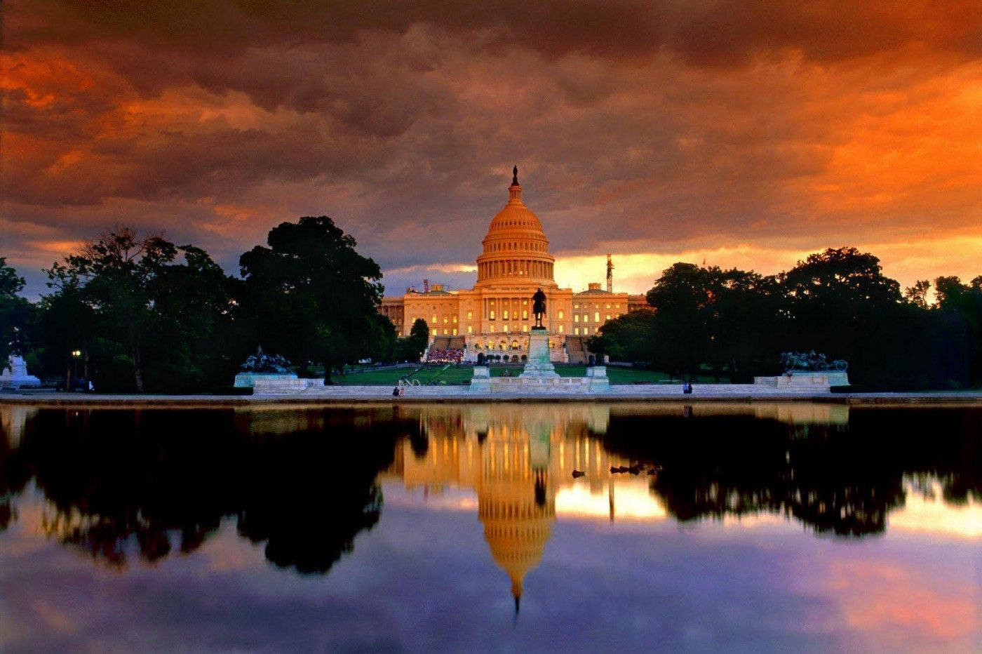 Washington 桌布 壁紙 — 美國國會大廈在日落時分溫暖地發光，其倒影在平靜的倒影池水面上閃爍，映襯著火紅的橙色和紫色天空。