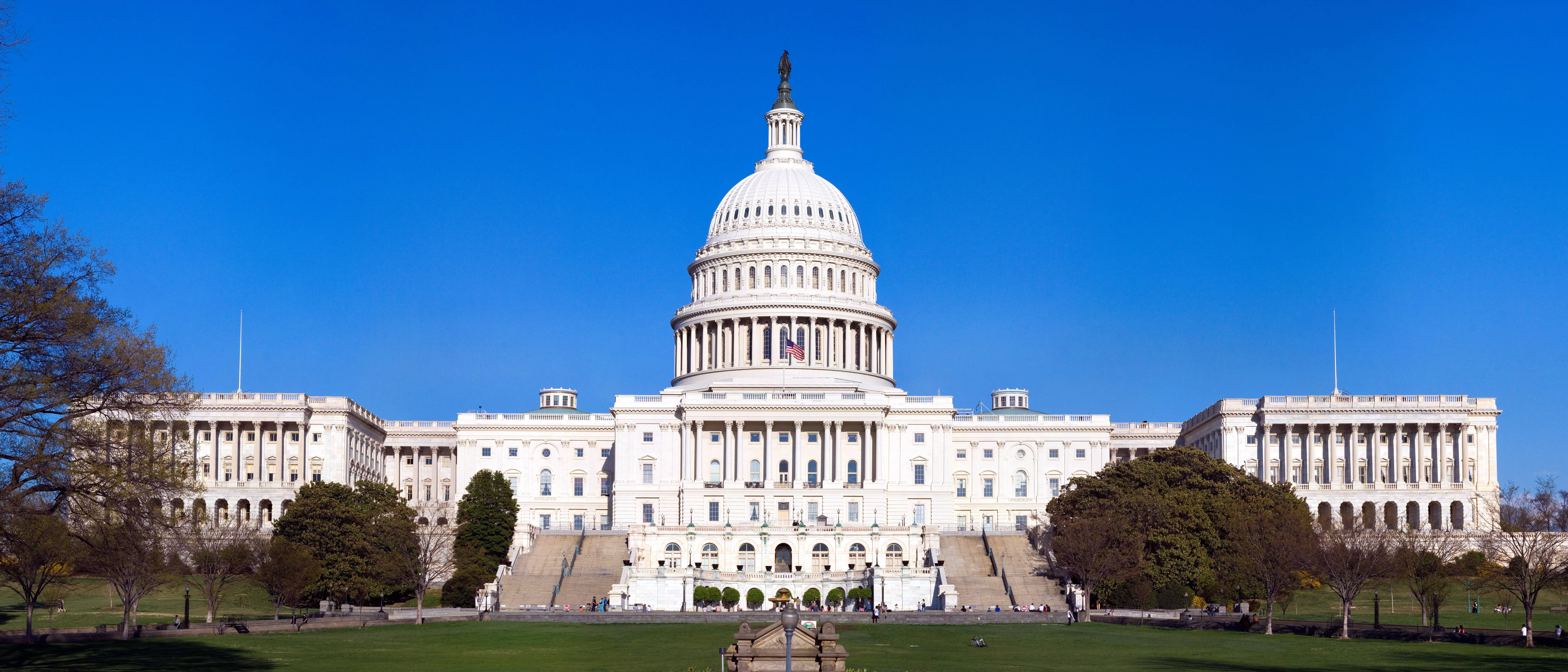 Washington 桌布 壁紙 — 美國國會大廈在晴朗的藍天下雄偉地矗立，鬱鬱蔥蔥的綠色草坪和樹木襯托著其宏偉的新古典主義建築。