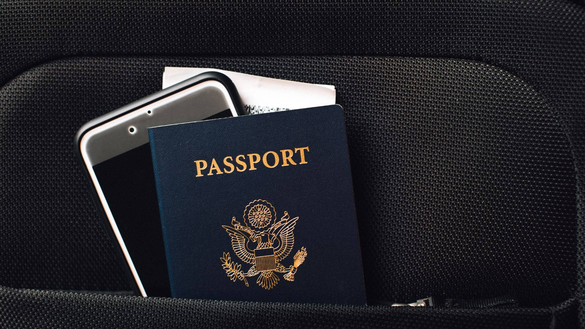 Passport 桌布 壁紙 — 美國護照和智慧型手機放在黑色紋理背包口袋中，準備旅行。