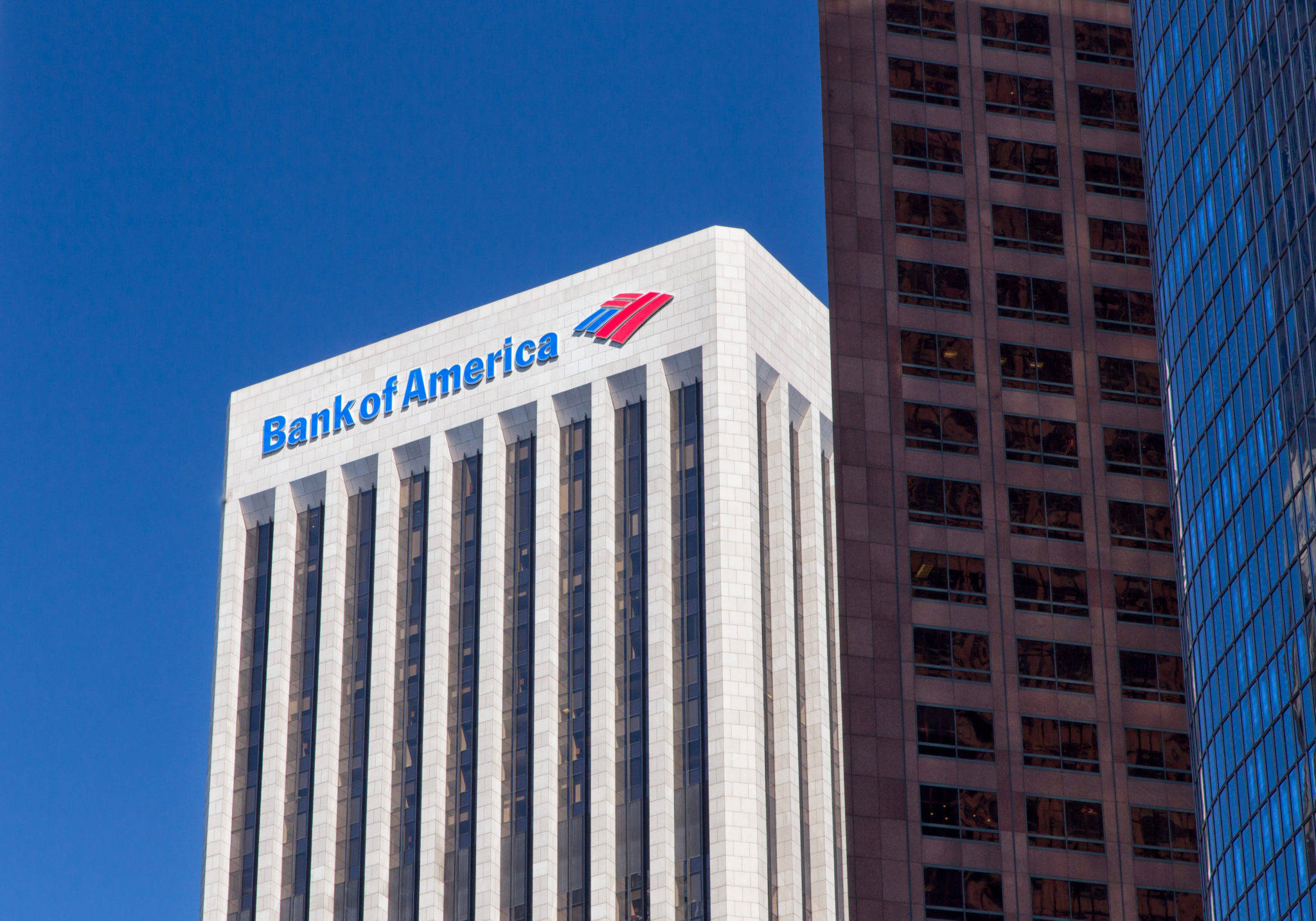 Bank 桌布 壁紙 — 美國銀行摩天大樓帶有藍色標誌，在晴朗的藍天下與玻璃和混凝土辦公大樓並立。