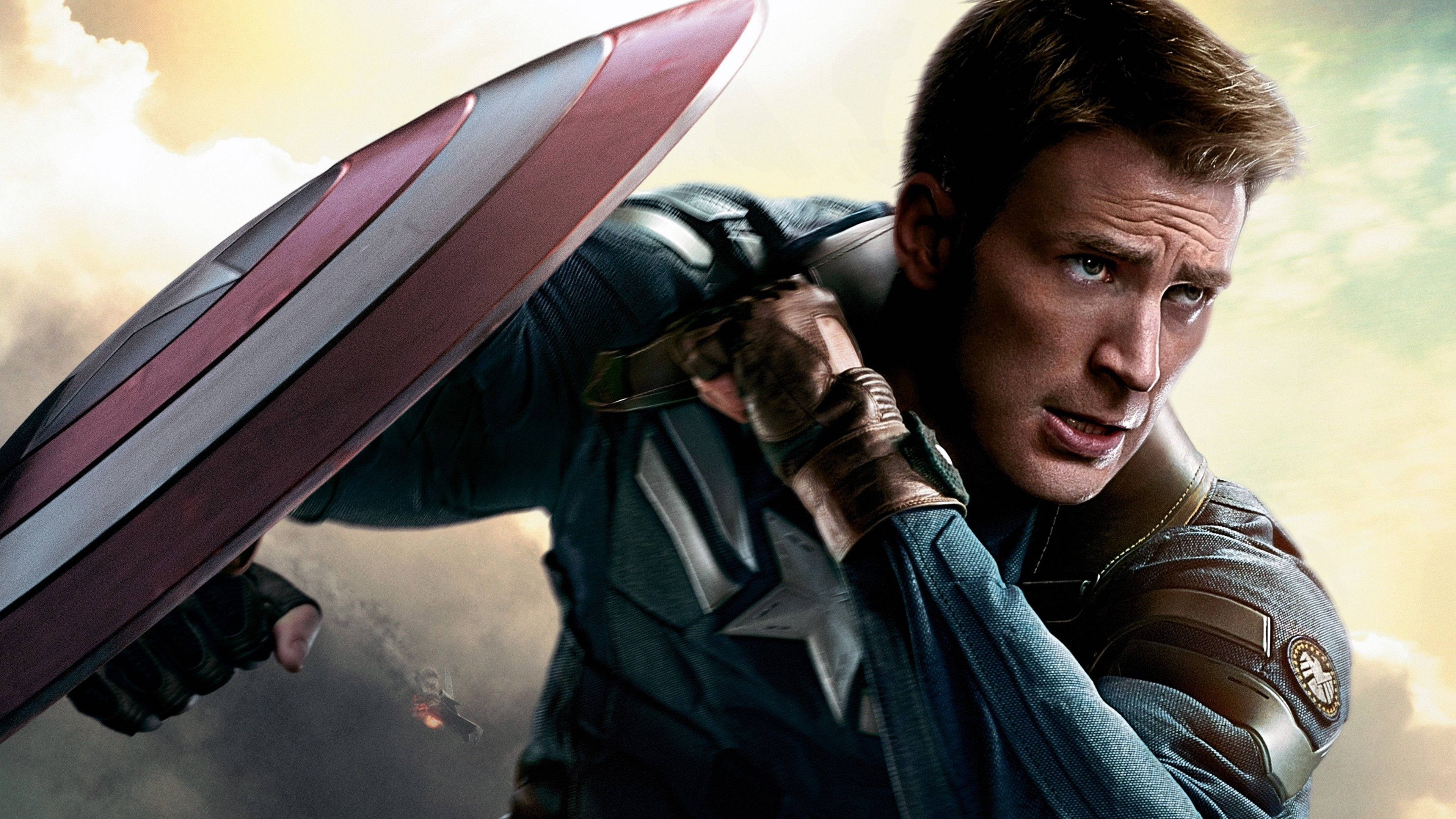Best Captain America 桌布 壁紙 — 美國隊長以動作姿勢手持標誌性盾牌，背景為多雲的天空。